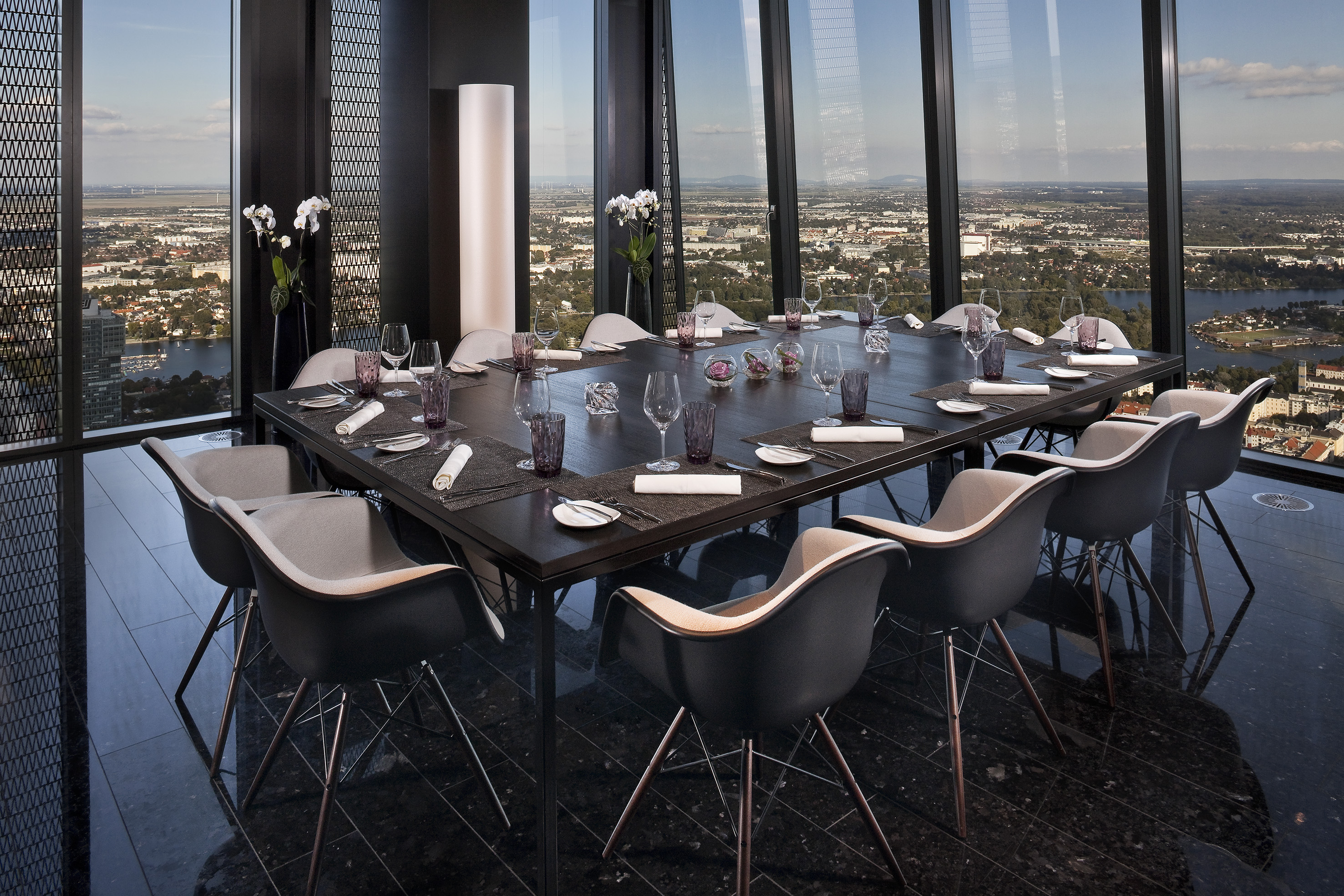 Panoramic high-rise dining room overlooking a city, with elegant table settings.
