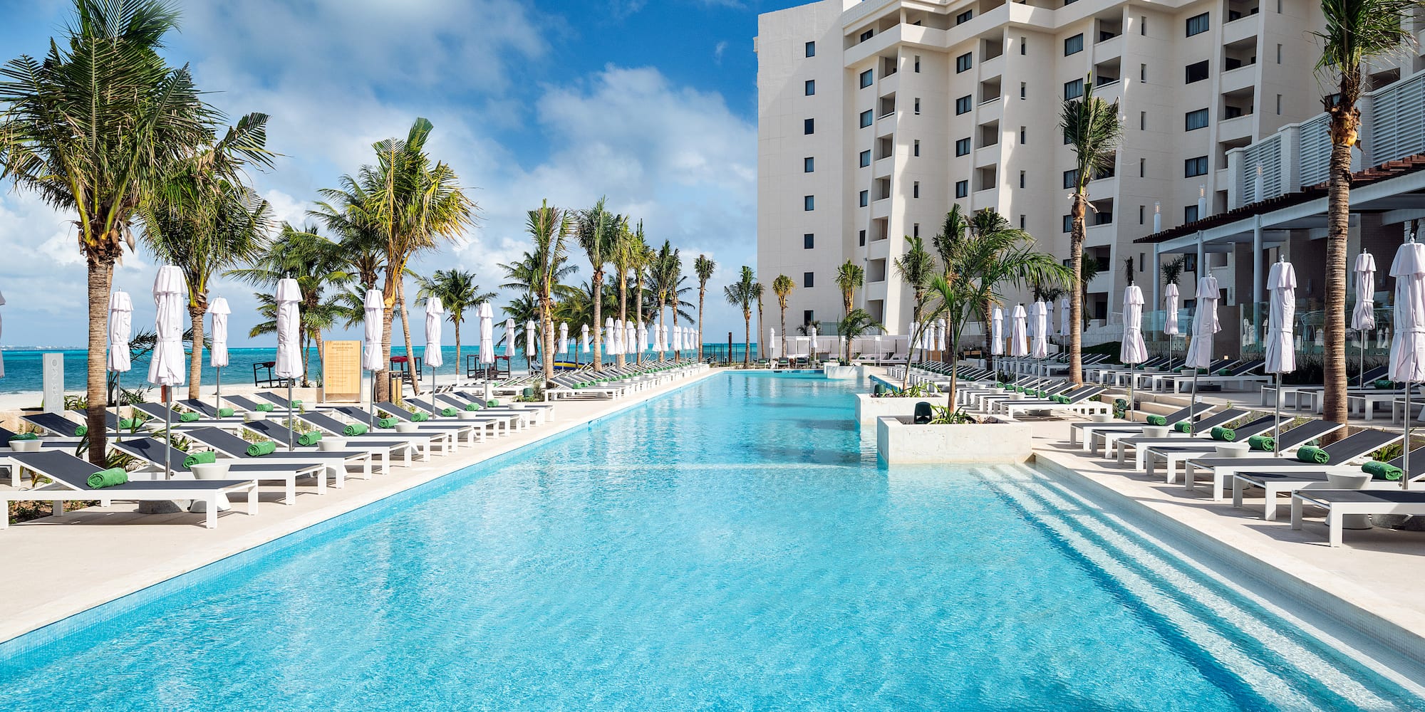 a pool with lounge chairs and palm trees in front of a building