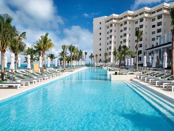 a pool with lounge chairs and palm trees in front of a building