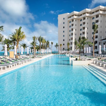 a pool with lounge chairs and palm trees in front of a building
