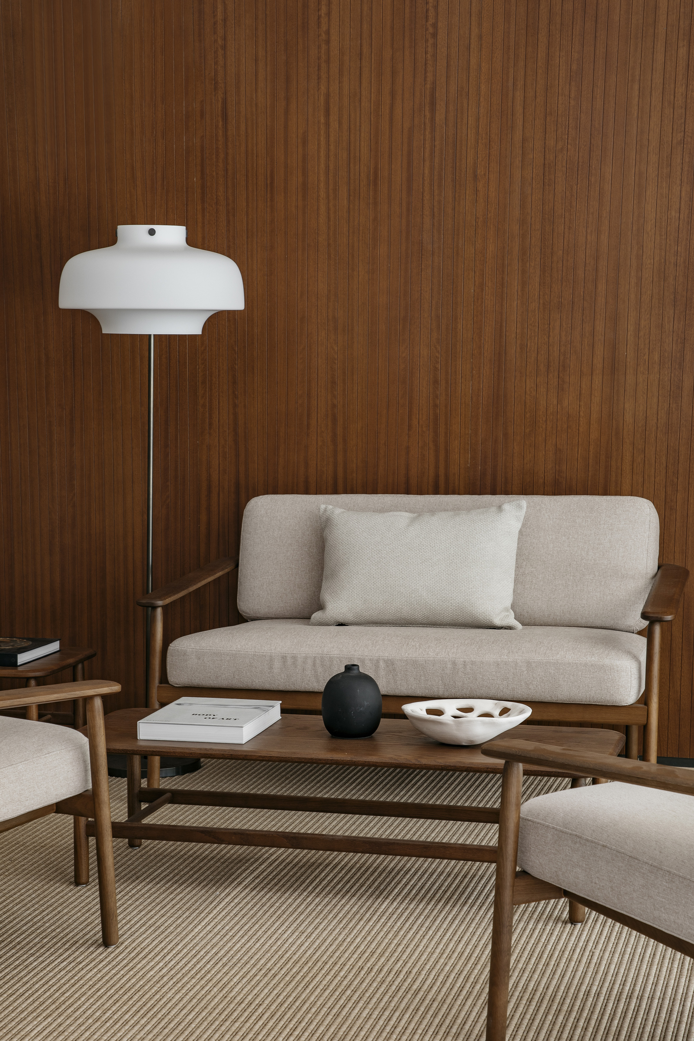Mid-century modern living room with wood paneling, beige sofa, coffee table, lamp.