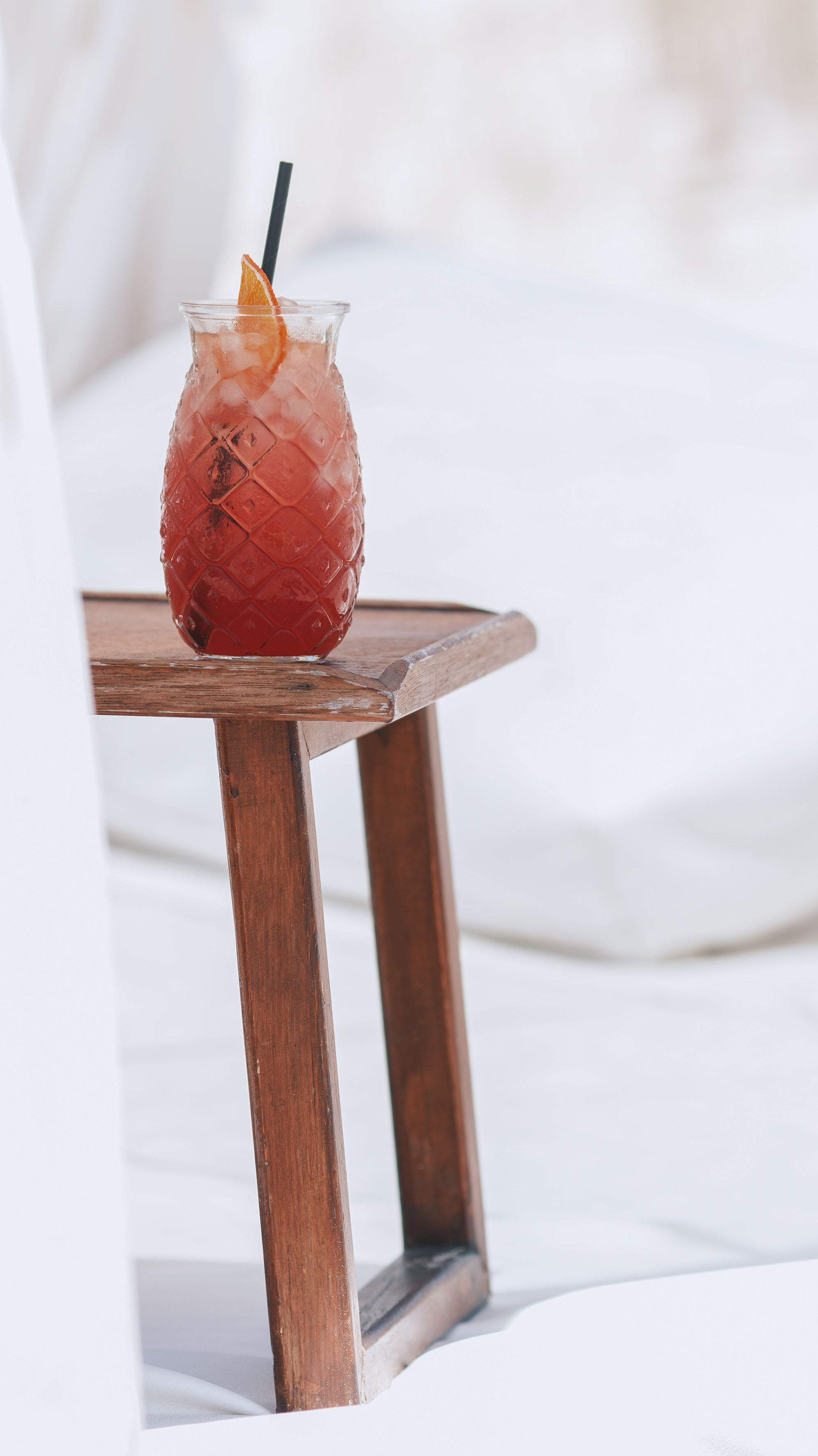 Red tropical cocktail in pineapple glass with orange on wooden table.