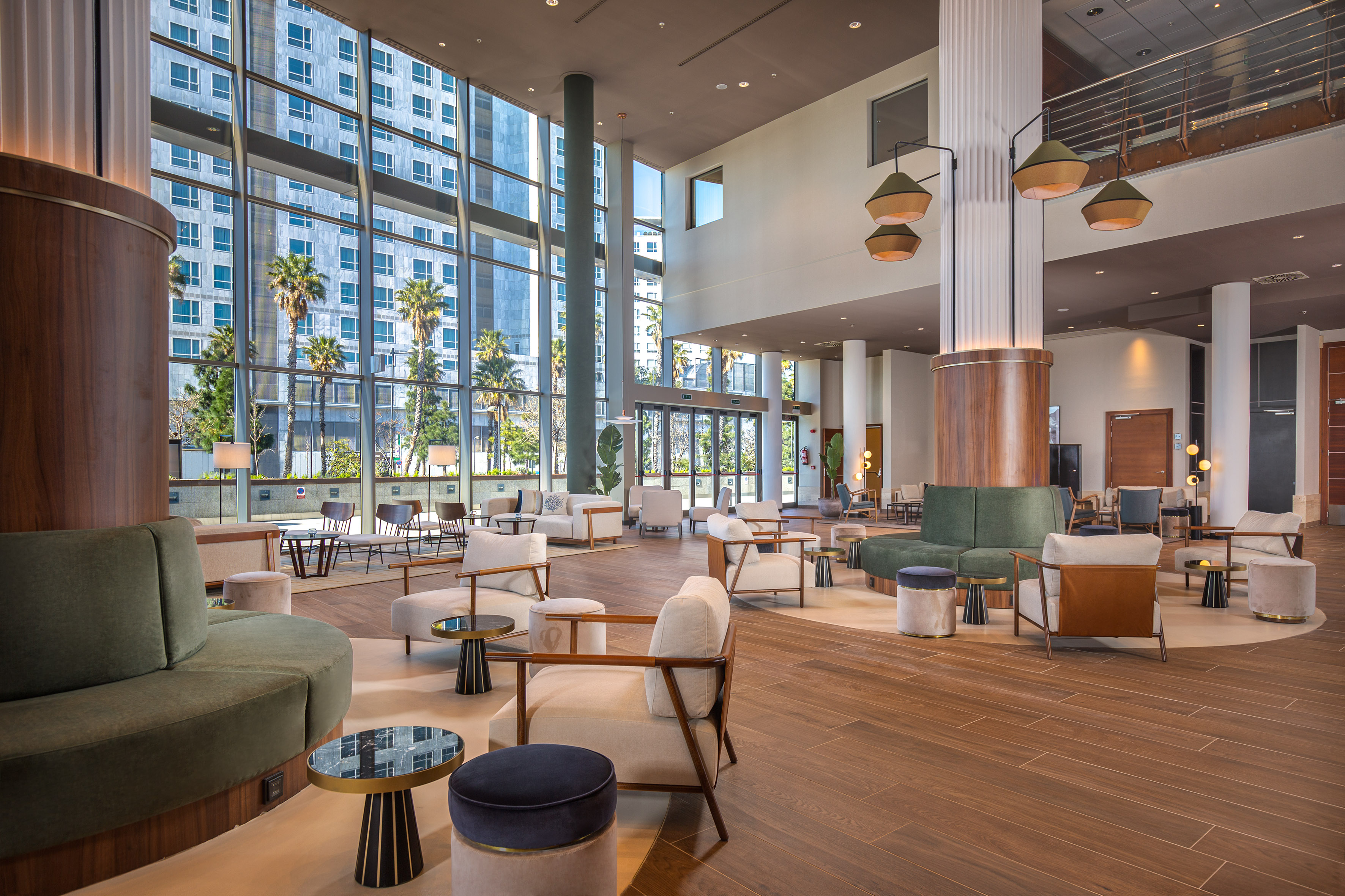 Modern hotel lobby with contemporary seating, large windows, and palm trees.
