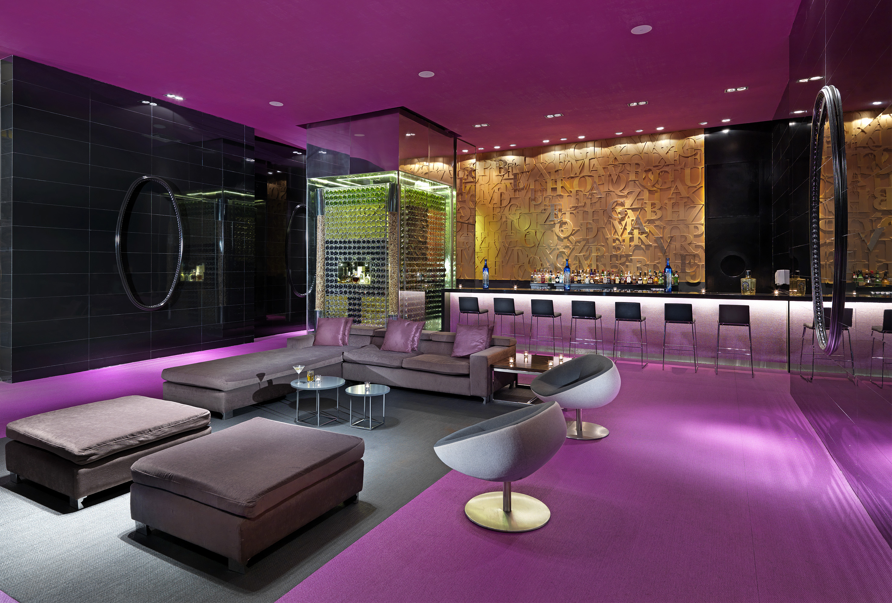Modern bar lounge with magenta lighting, glass wine cellar, and contemporary seating.