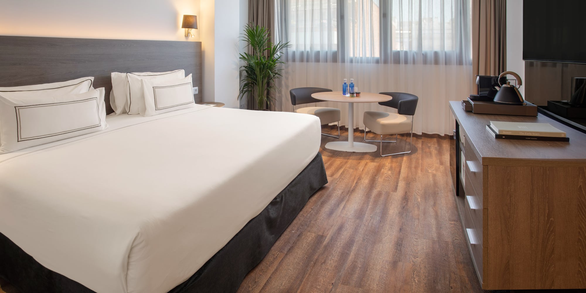 Contemporary hotel room with comfortable bed, wooden floor, and seating area.