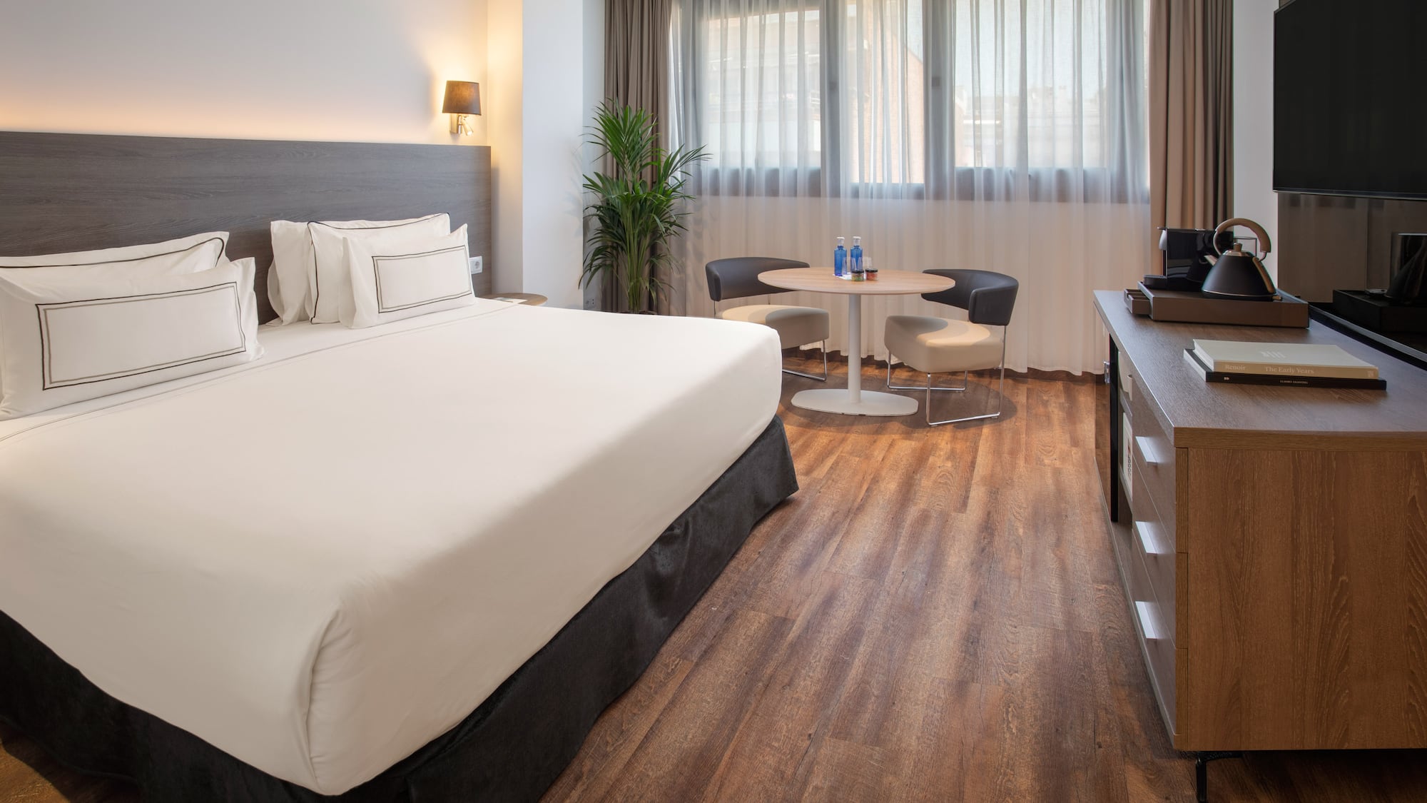 Contemporary hotel room with comfortable bed, wooden floor, and seating area.