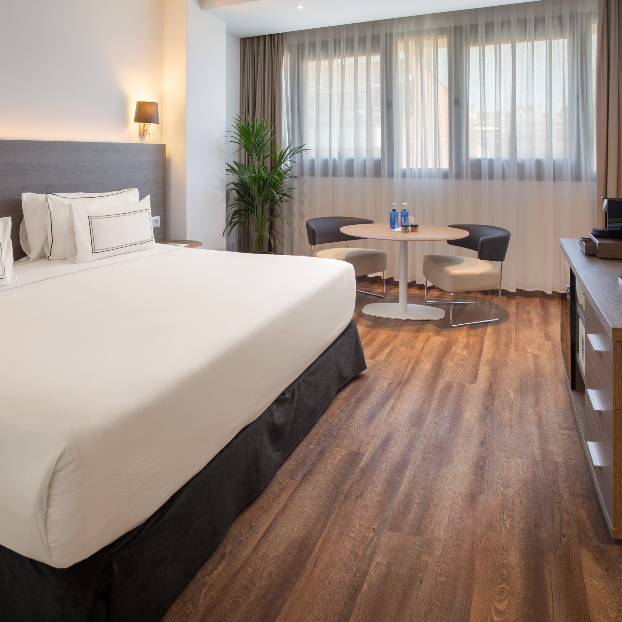Modern hotel room with comfortable bed, sitting area, wood floor, and window.