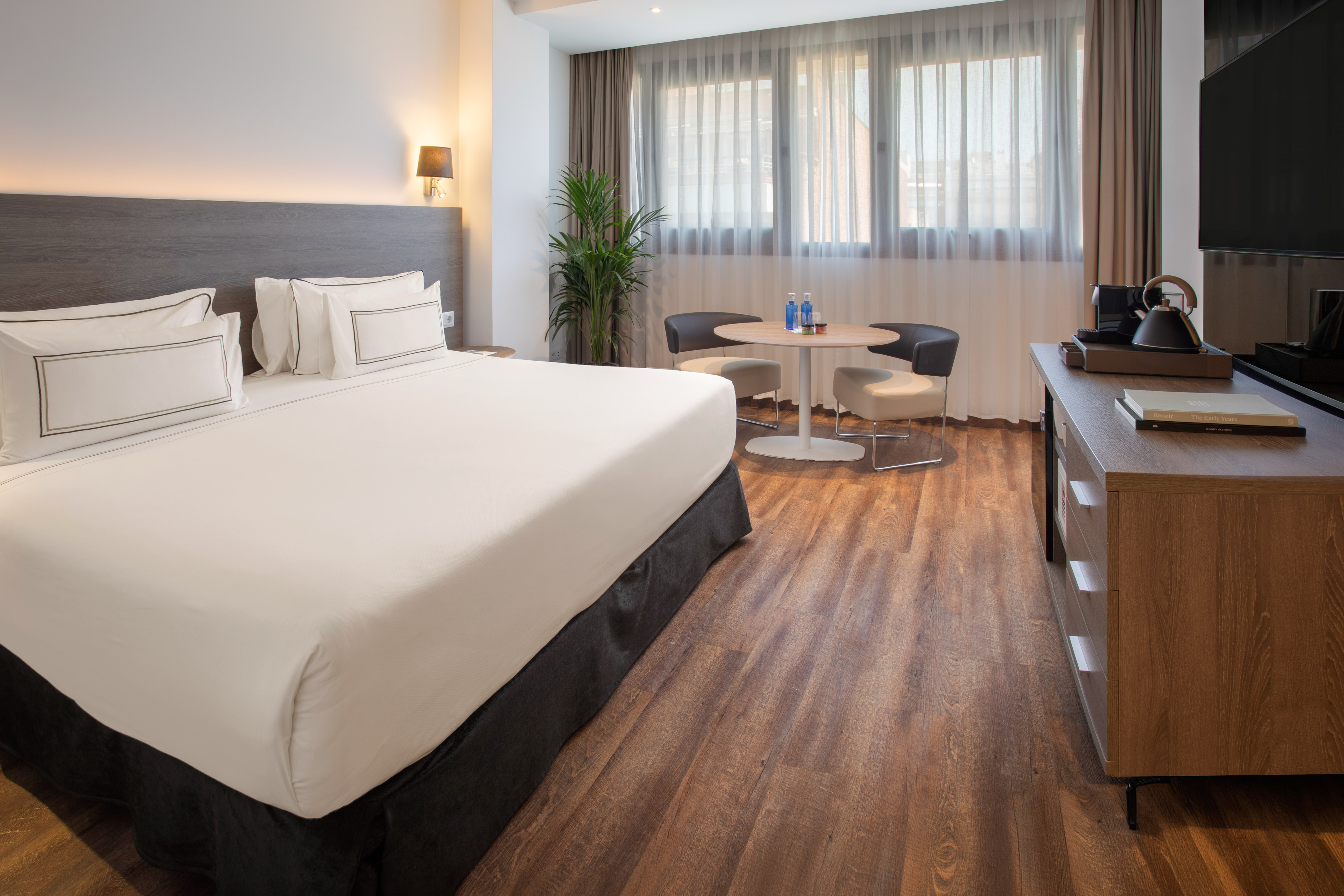 Contemporary hotel room with comfortable bed, wooden floor, and seating area.