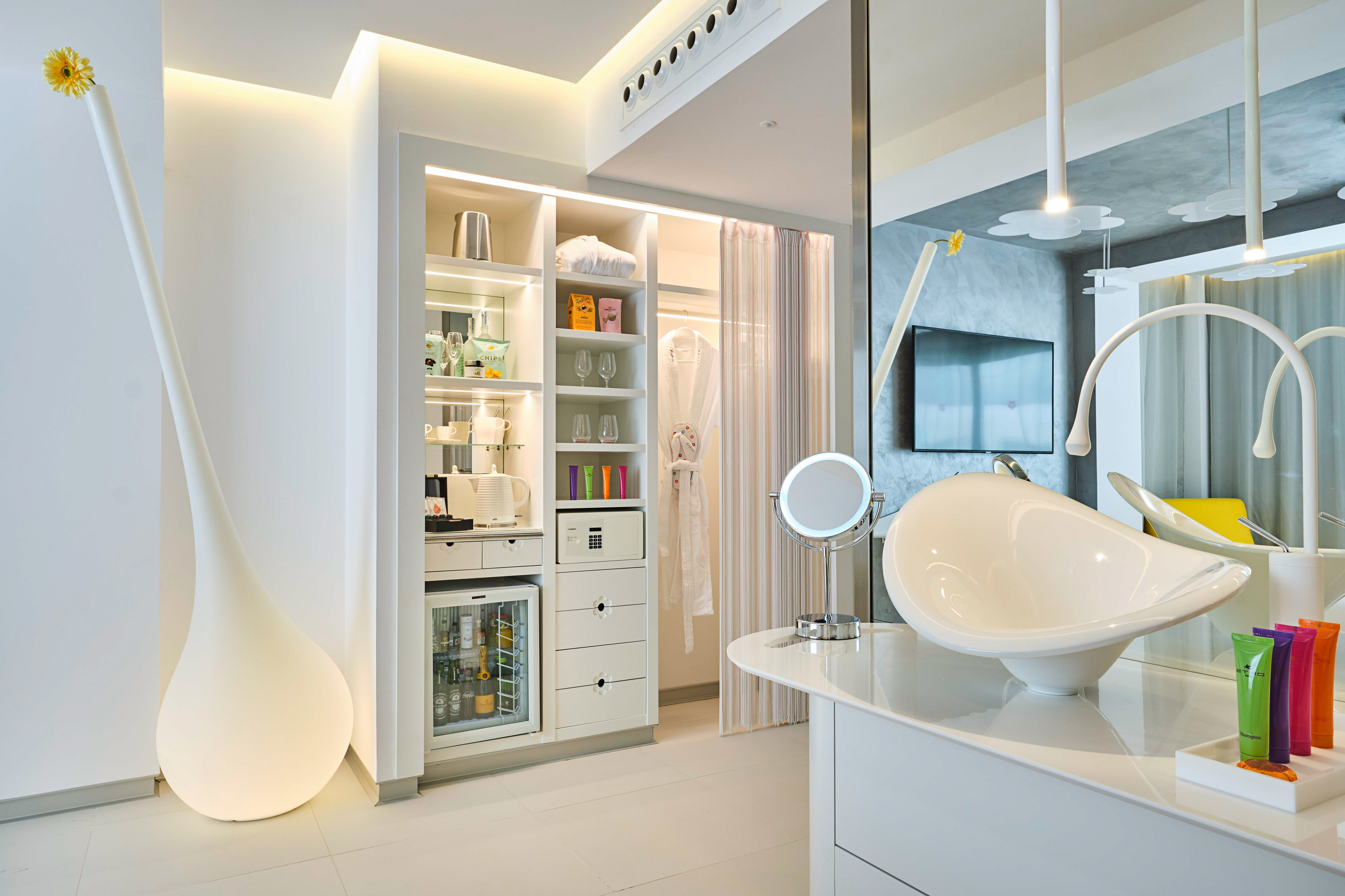 Modern white hotel suite with built-in storage, mini-bar, and vanity.