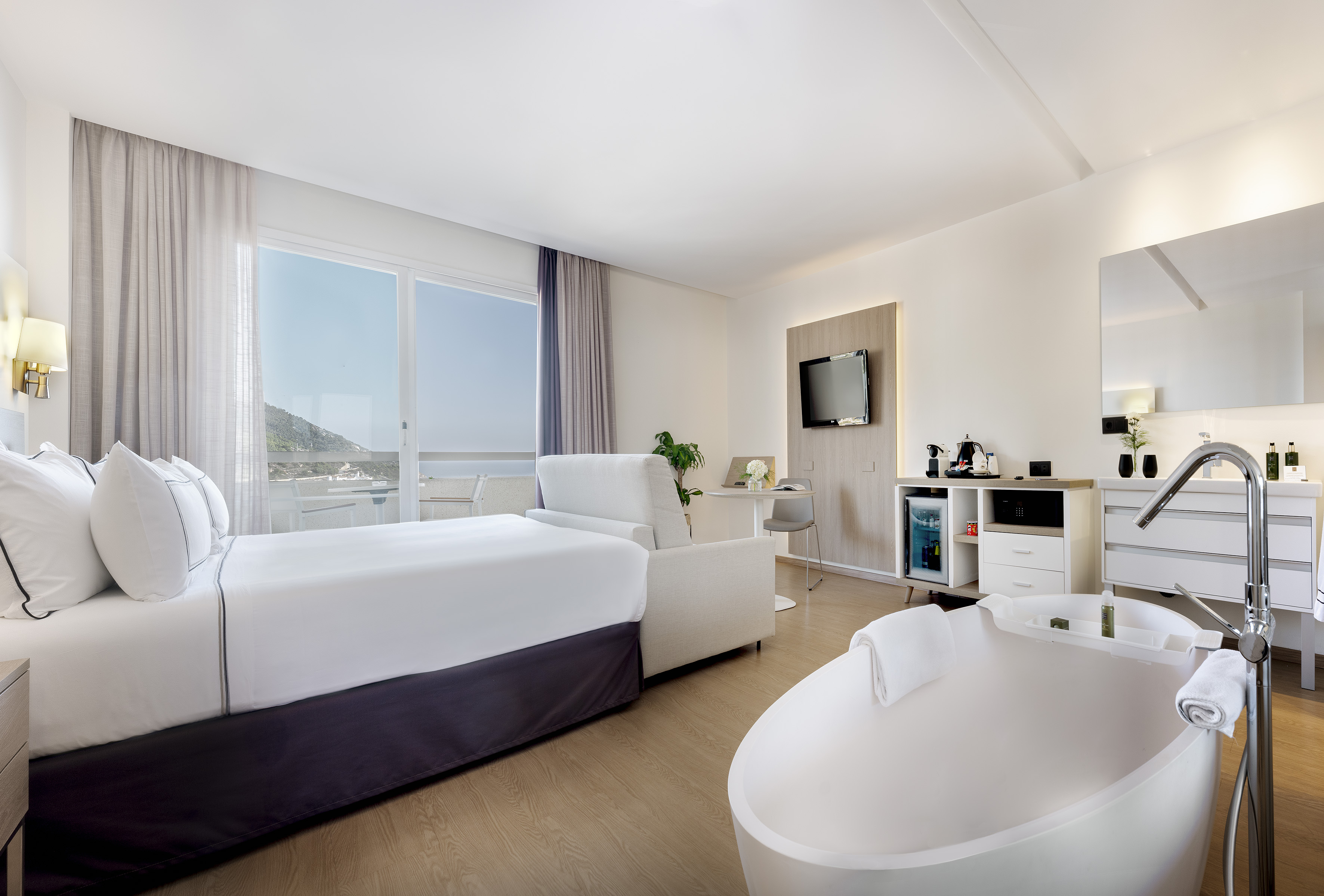 Luxury hotel suite with balcony sea view, large bed, and freestanding tub.