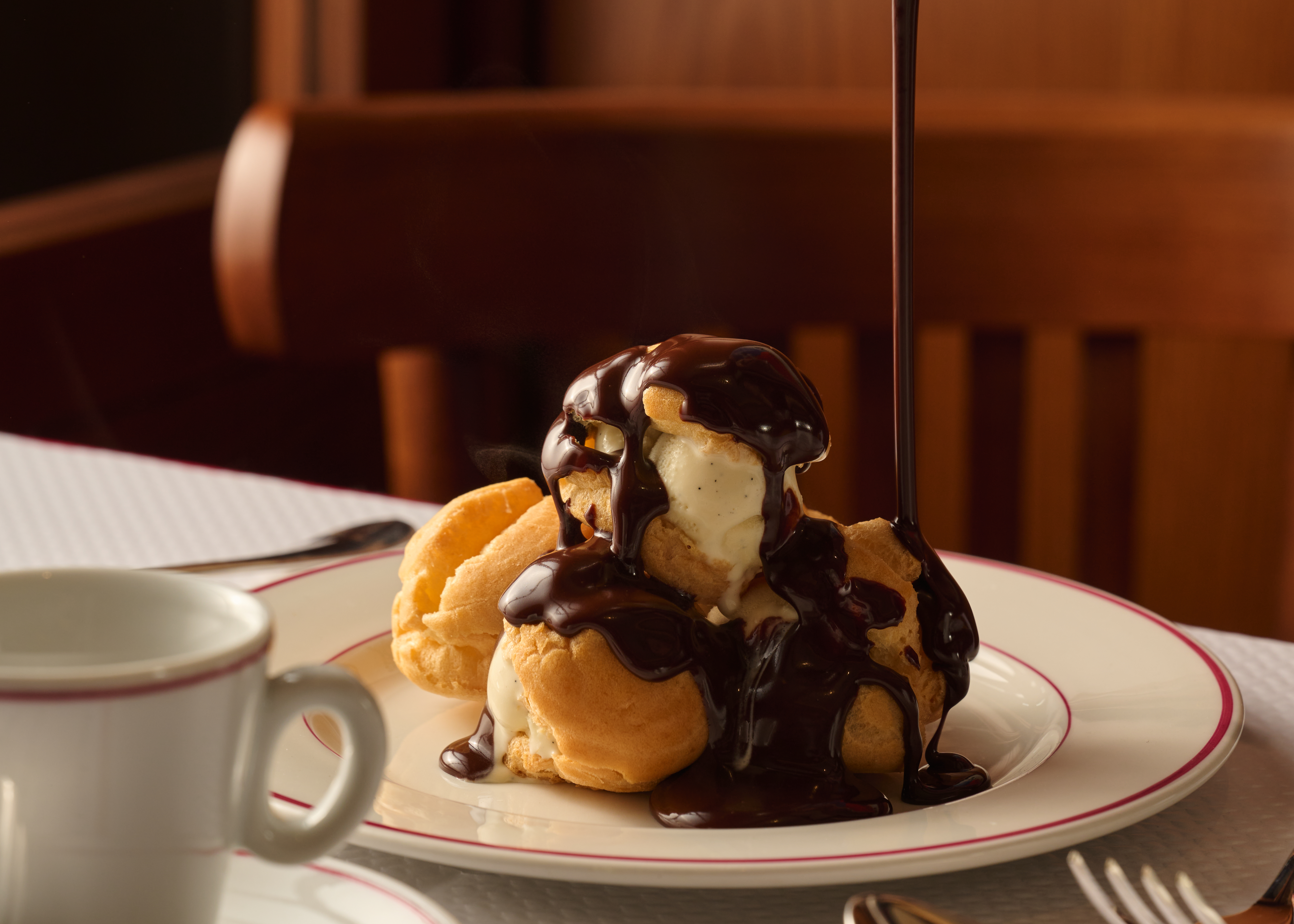 Profiteroles with vanilla ice cream and warm chocolate sauce pouring over them.