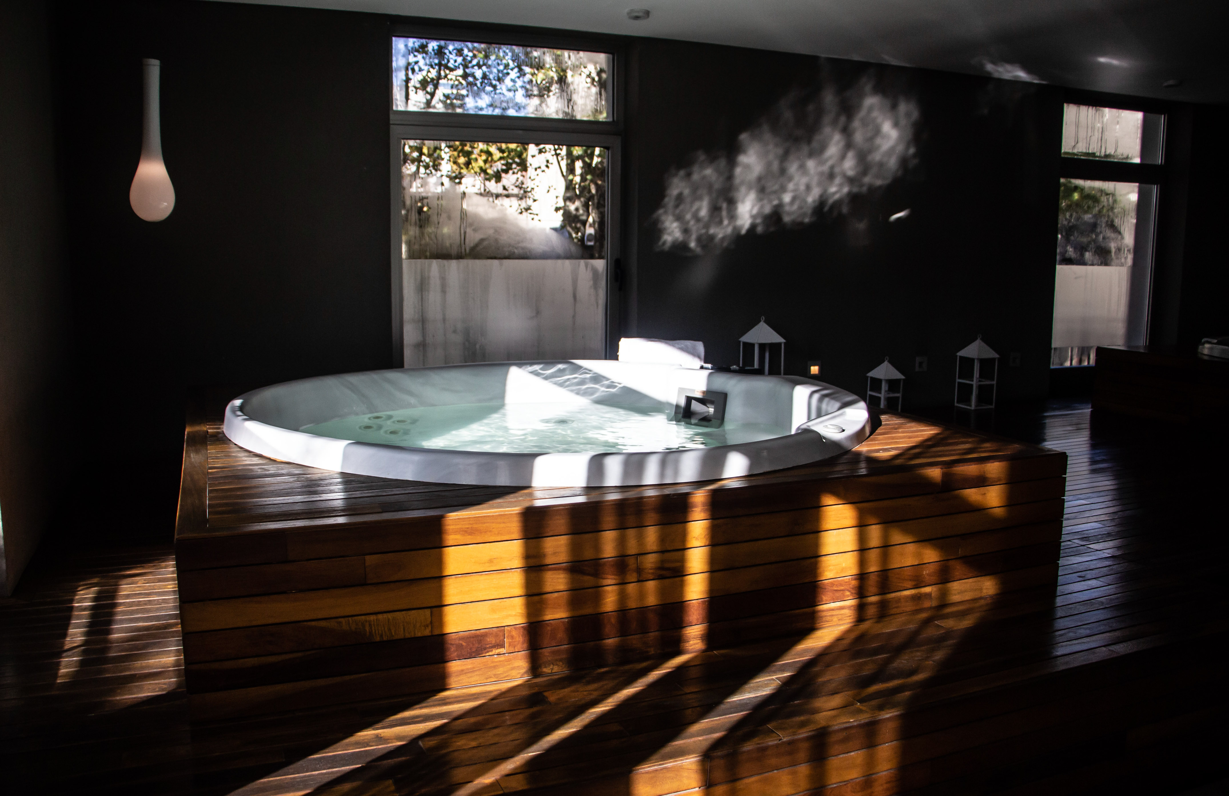 Modern hot tub with steam, wooden deck, and sunlight in a dark spa room.