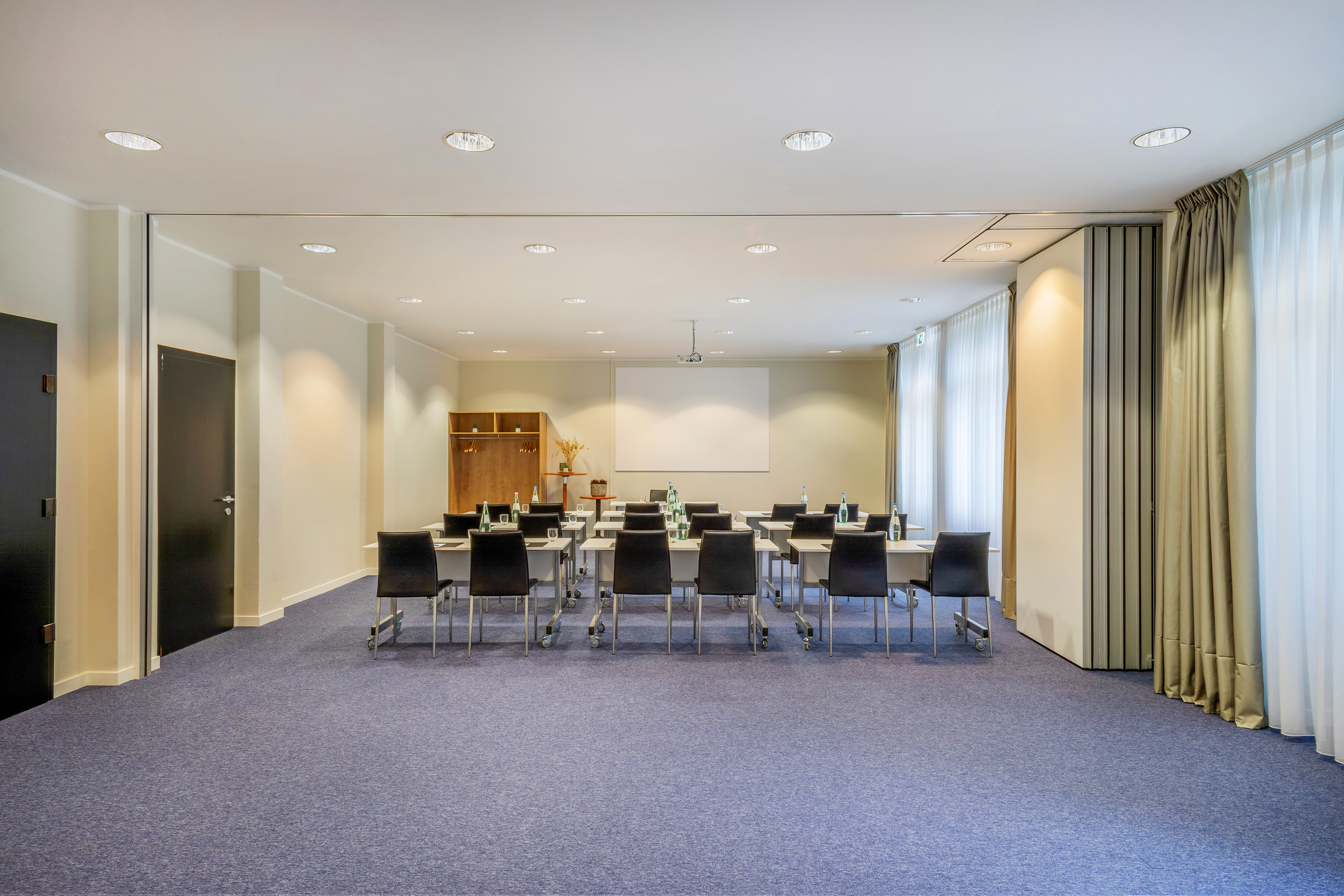 Spacious modern conference room with classroom setup, blue carpet, and screen.