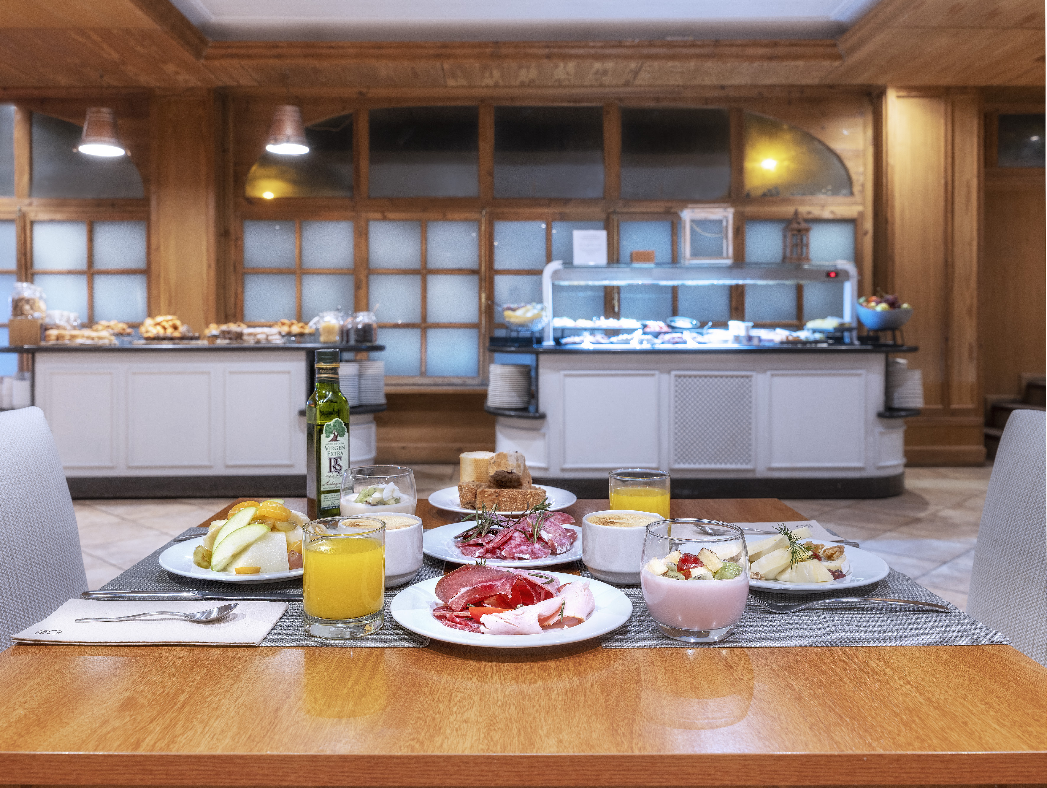 Hotel breakfast buffet: meats, fruit, juices, yogurts, pastries, olive oil.
