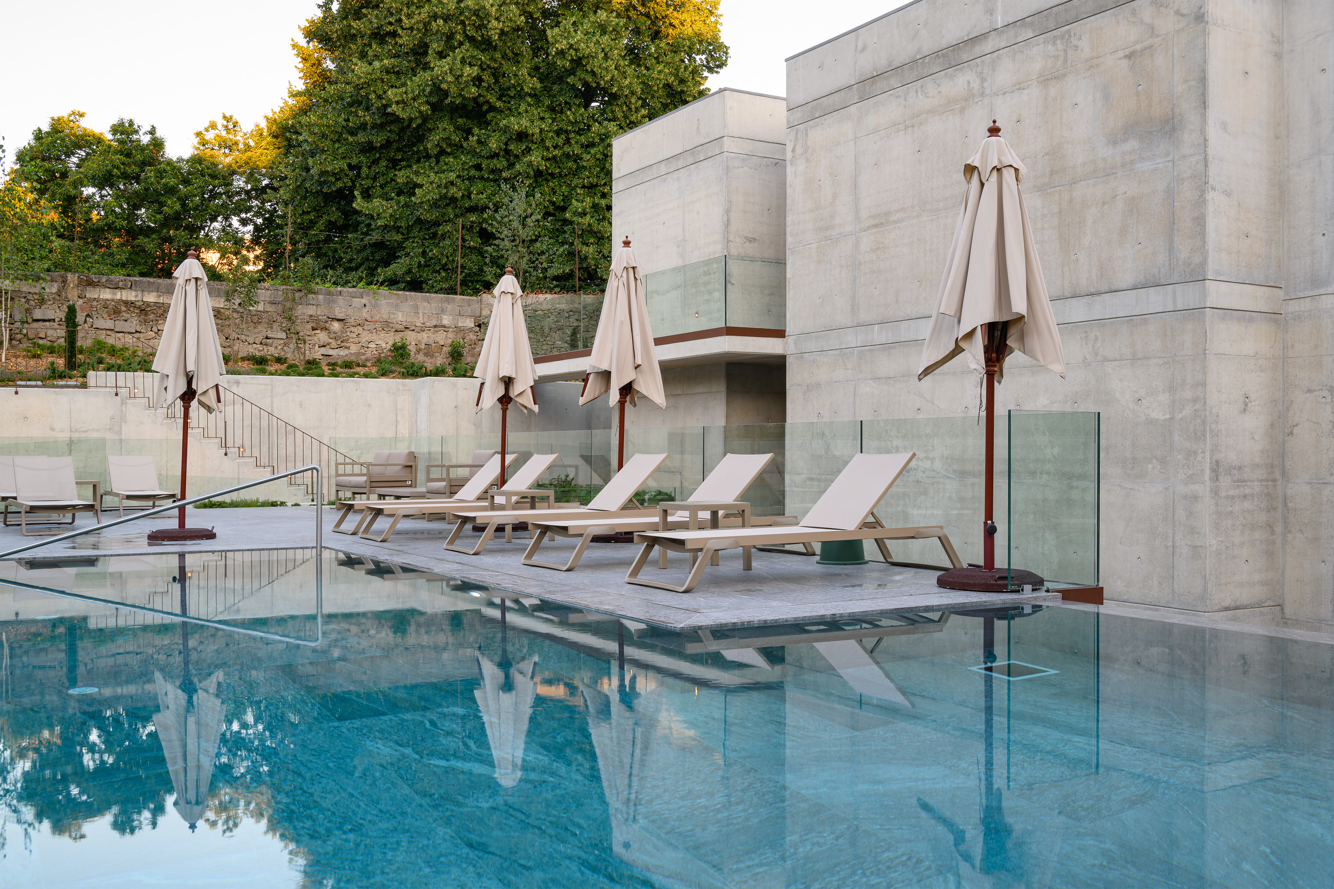 Modern resort pool with loungers, closed parasols, and concrete buildings.