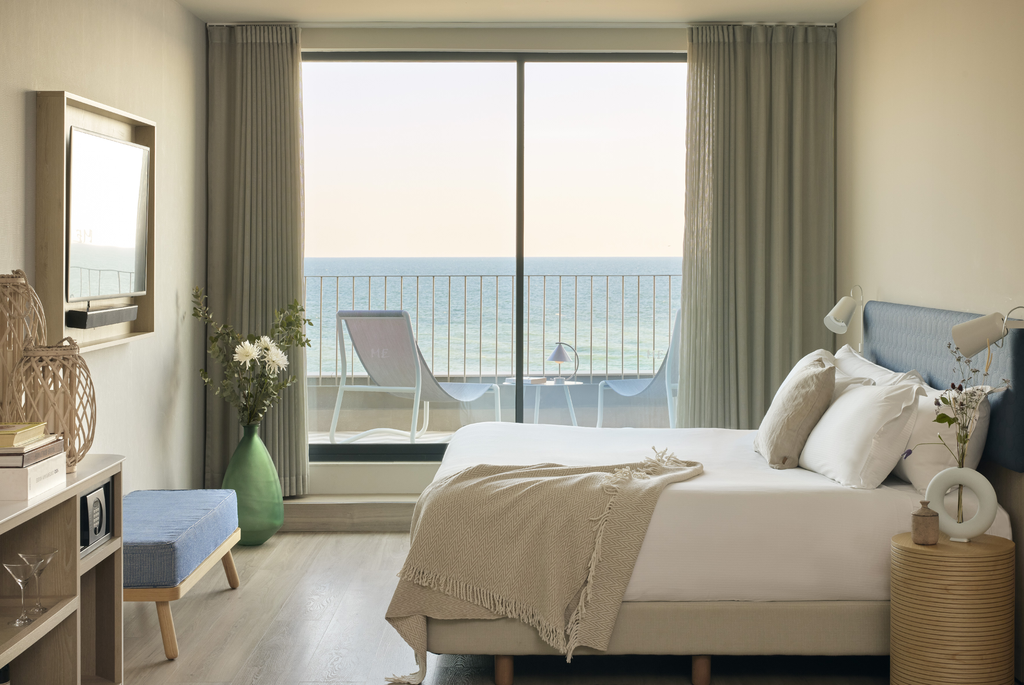 Modern hotel bedroom with ocean view balcony and lounge chairs.