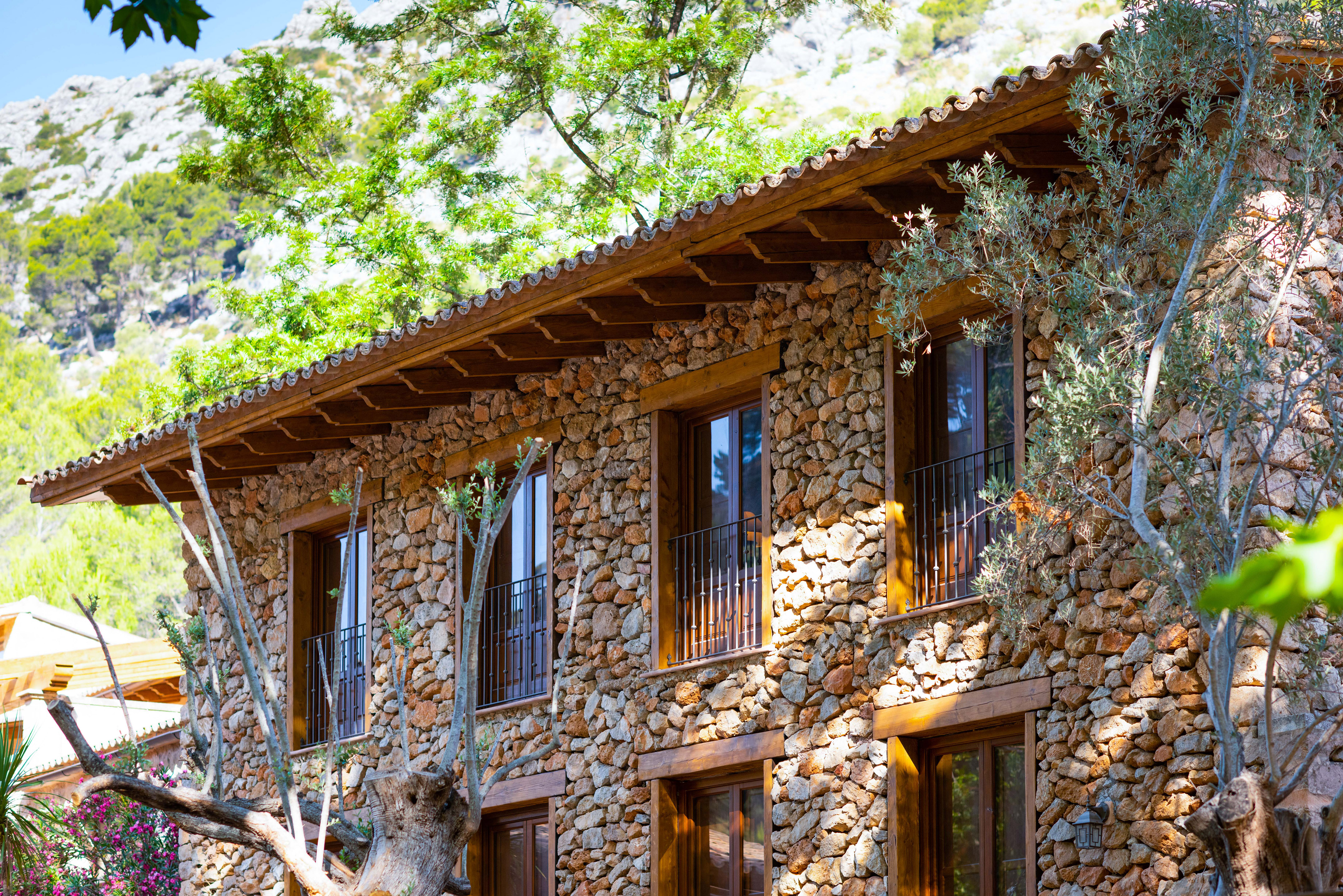 Rustic stone house with wood windows, balconies, tile roof, mountains.