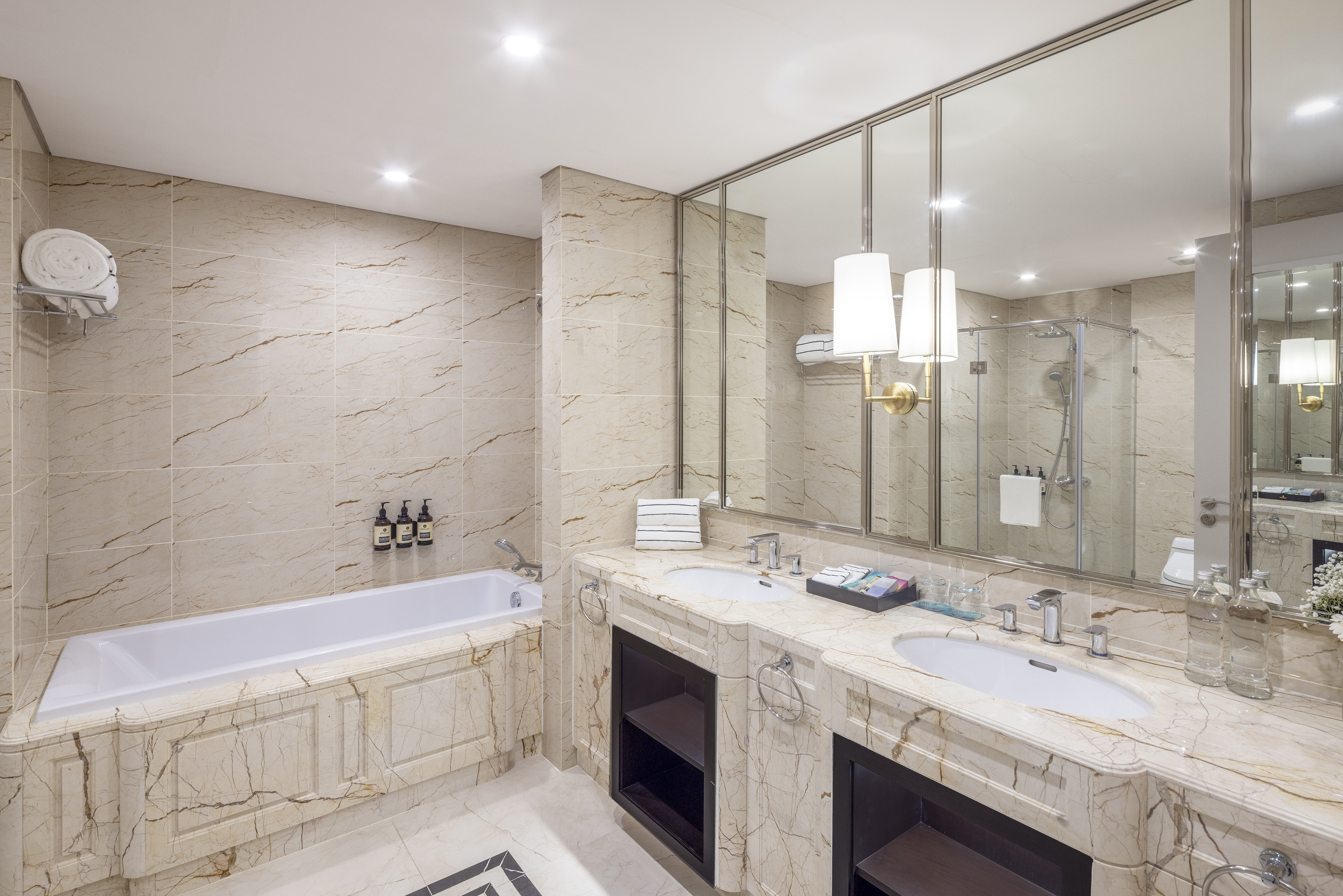 Modern marble hotel bathroom with bathtub, glass shower, and dual sinks.