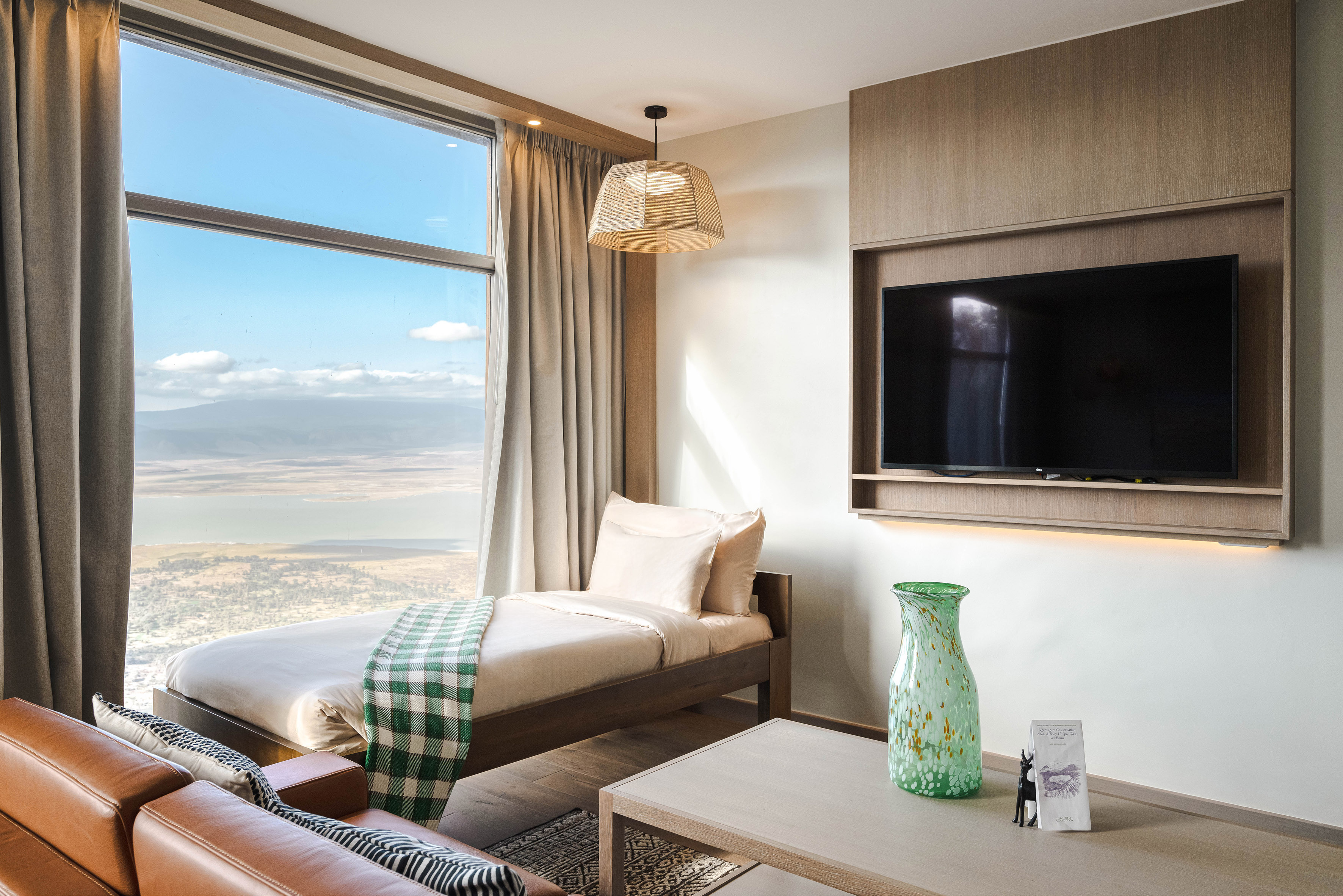 Hotel room with panoramic lake and mountain view, cozy bed, and sofa.