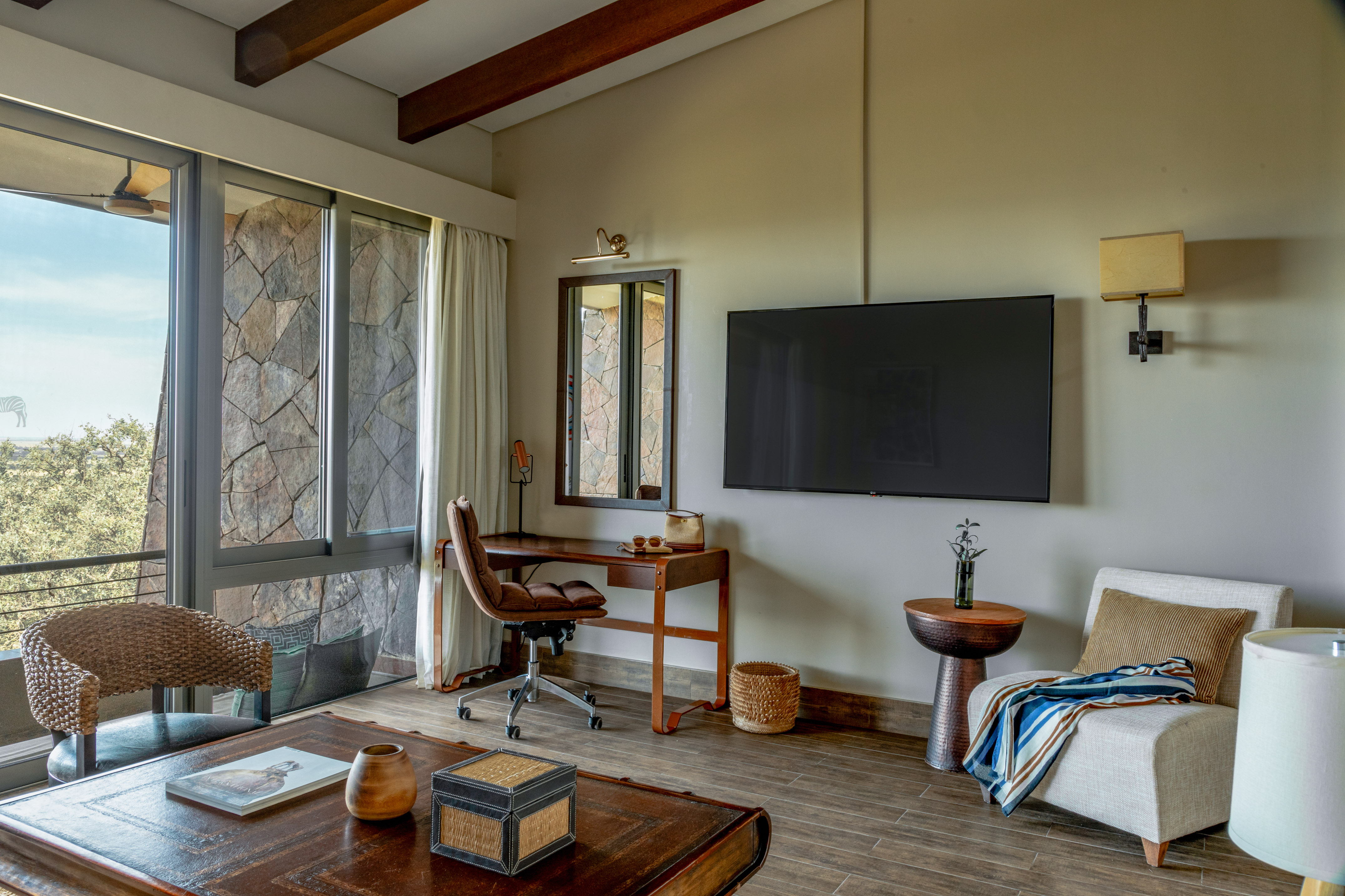 Comfortable safari lodge living area with desk, TV, and nature view.