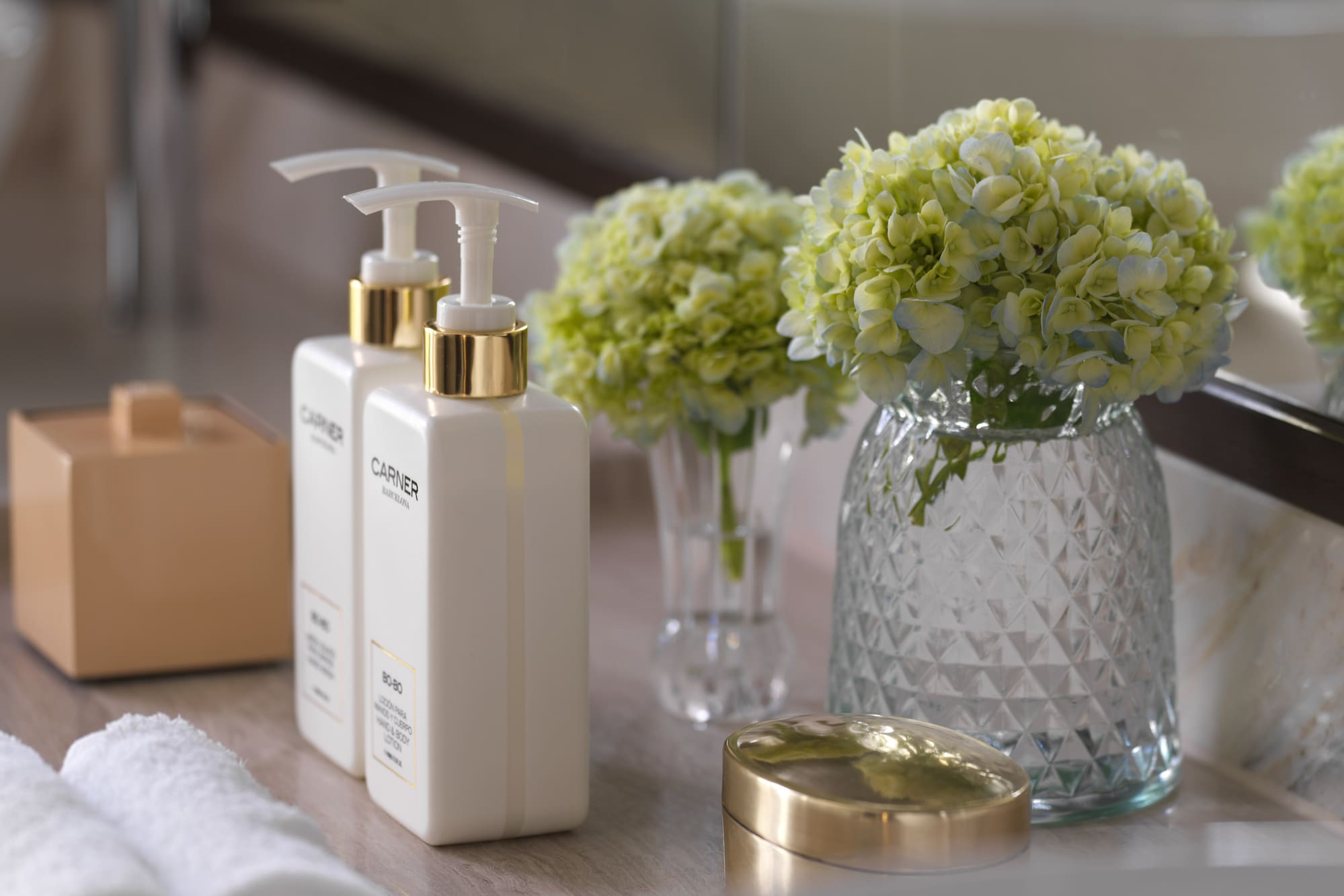 a group of white bottles with a gold lid next to a vase of flowers