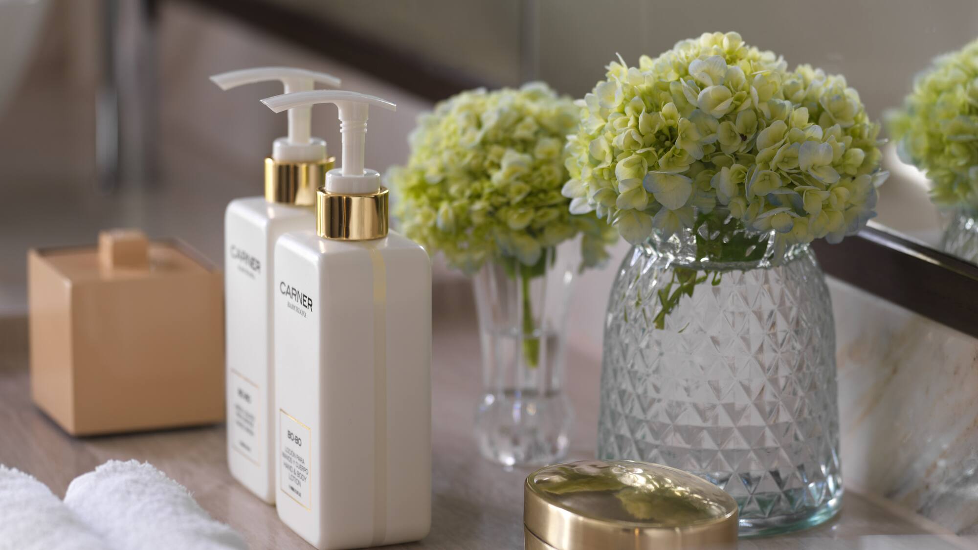 a group of white bottles with a gold lid next to a vase of flowers