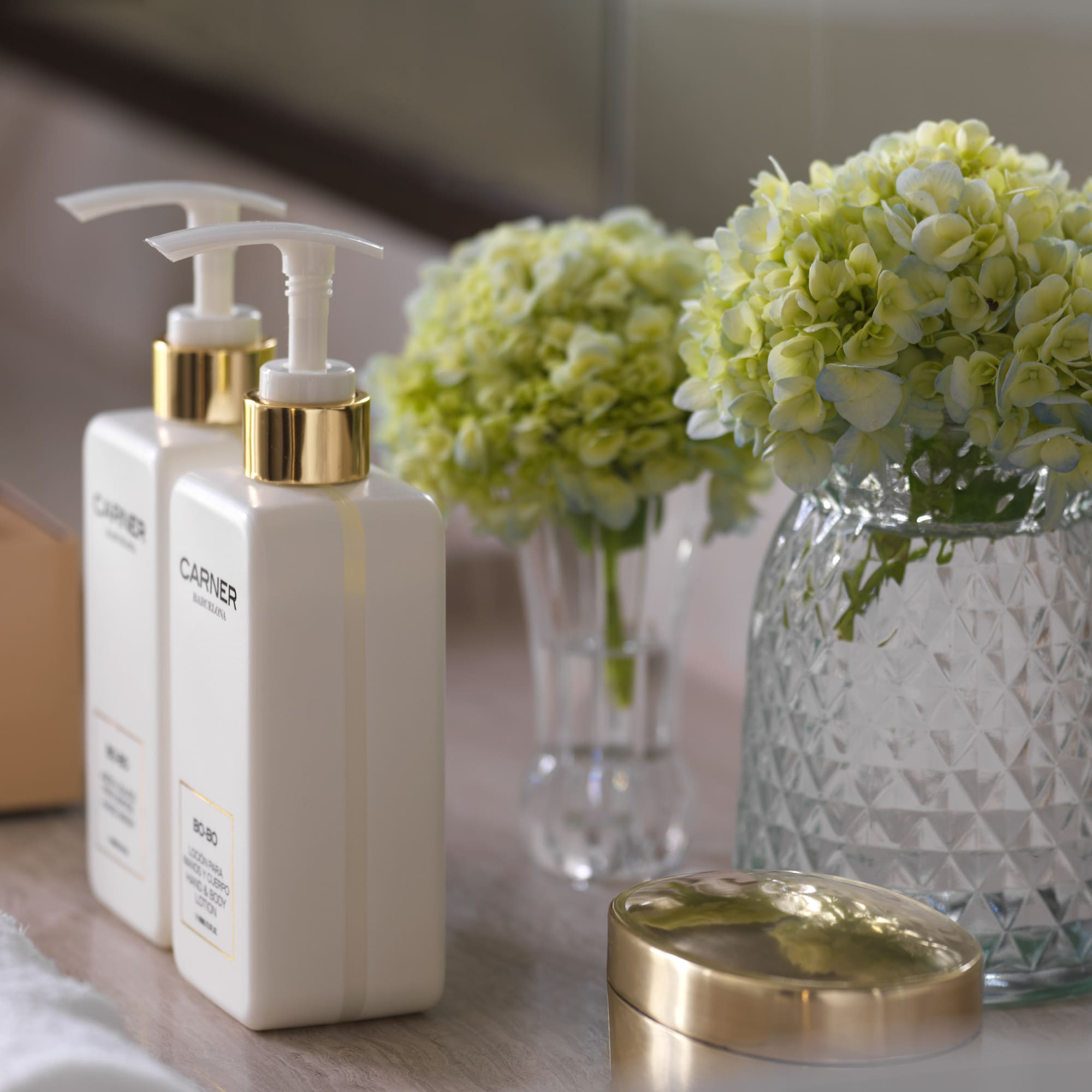 a group of white bottles with a gold lid next to a vase of flowers
