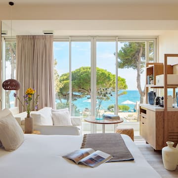 a room with a bed and a table and chairs and a window with trees and water