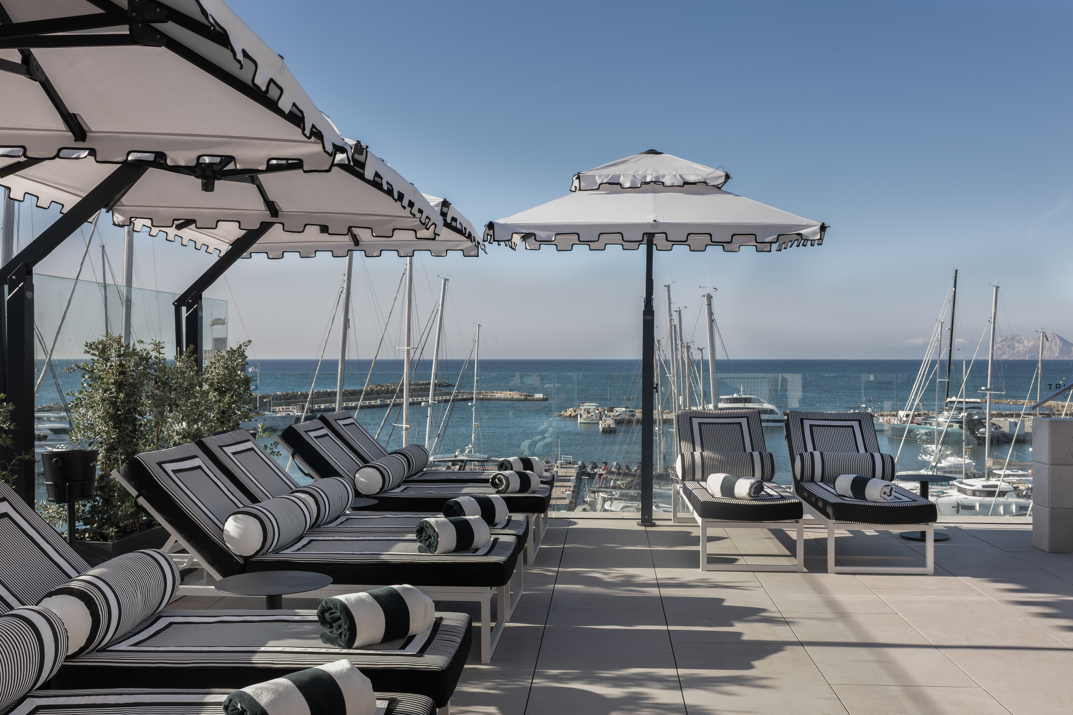 Luxury marina terrace with striped lounge chairs, umbrellas, and yachts.