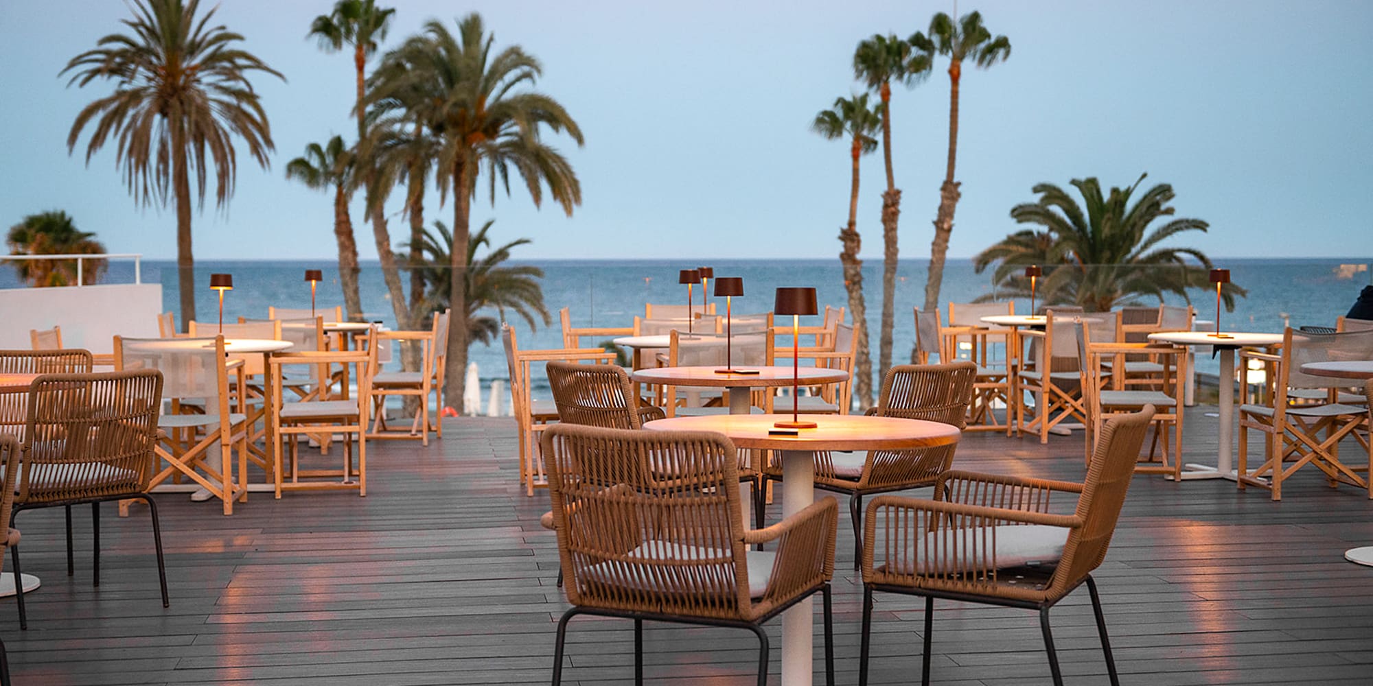 a table and chairs on a deck with palm trees and water in the background