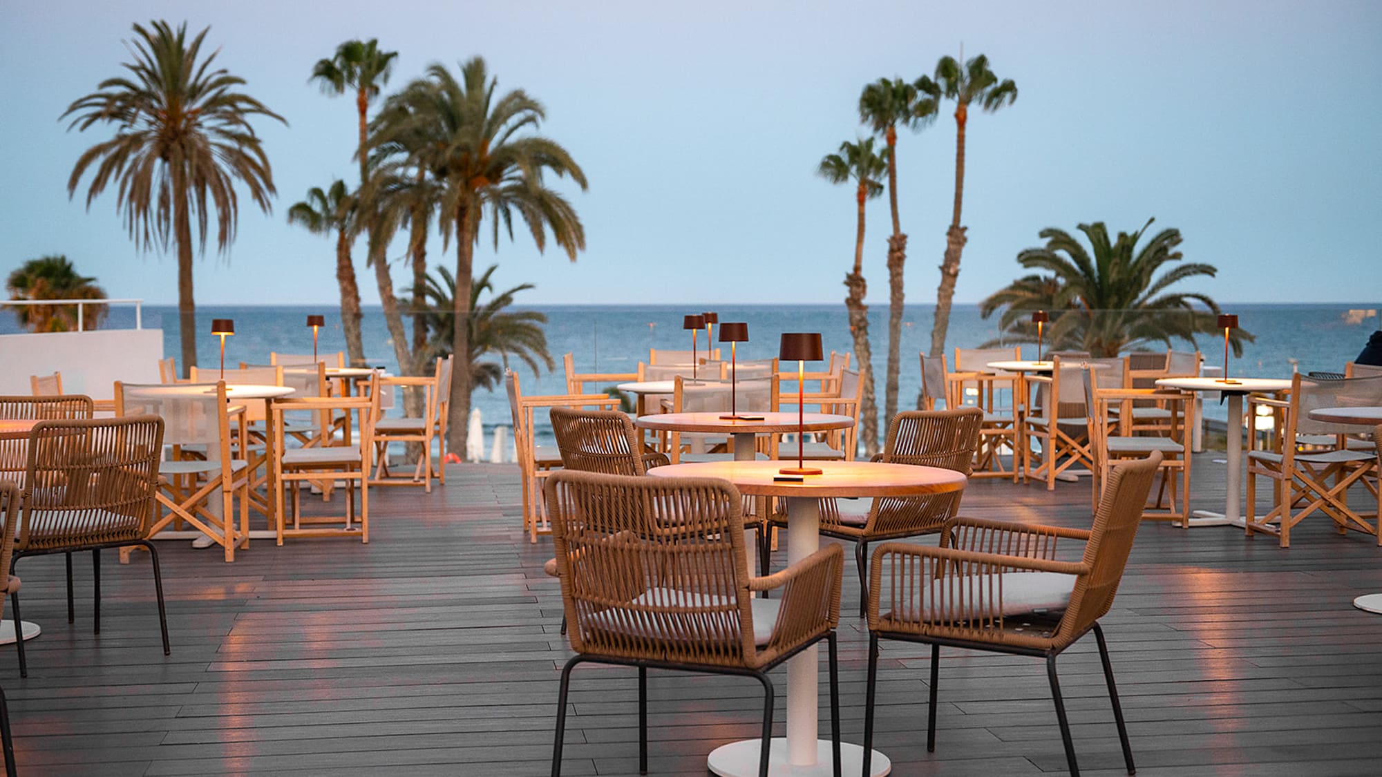 a table and chairs on a deck with palm trees and water in the background