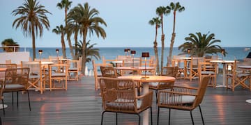 a table and chairs on a deck with palm trees and water in the background