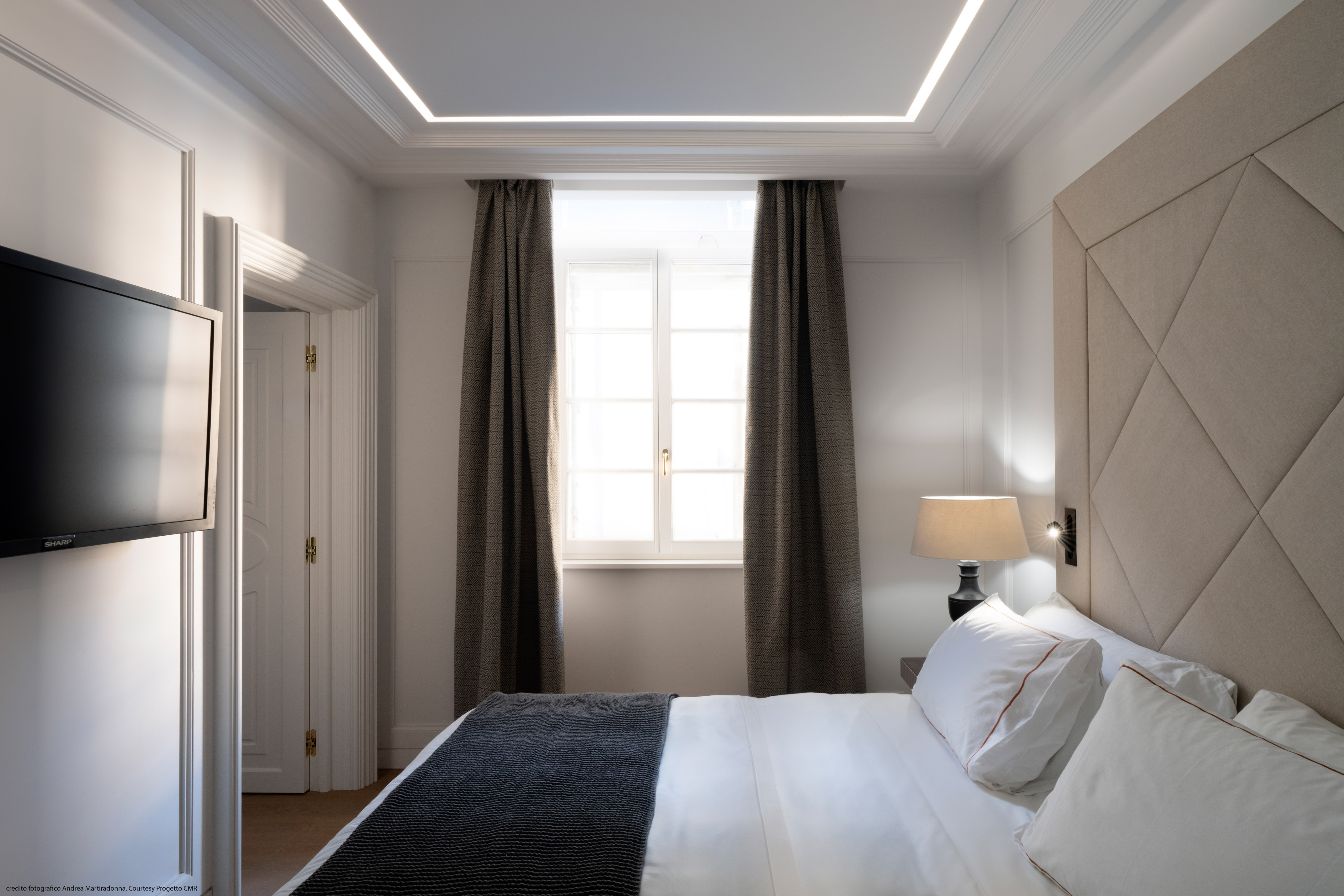 Elegant modern bedroom with geometric headboard, recessed lighting, and bright window.