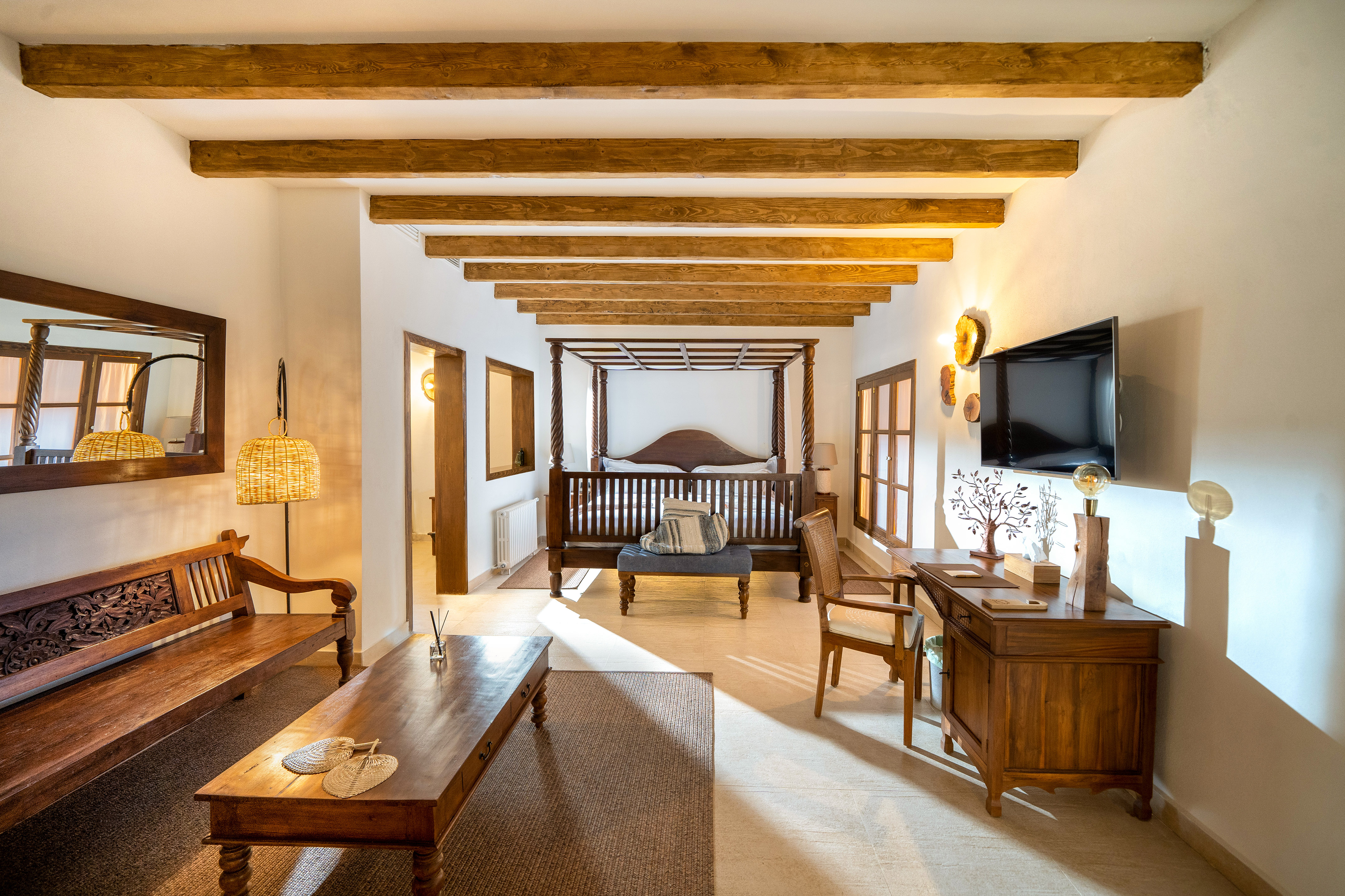 Warm rustic bedroom with four-poster bed, exposed beams, and dark wood furniture.