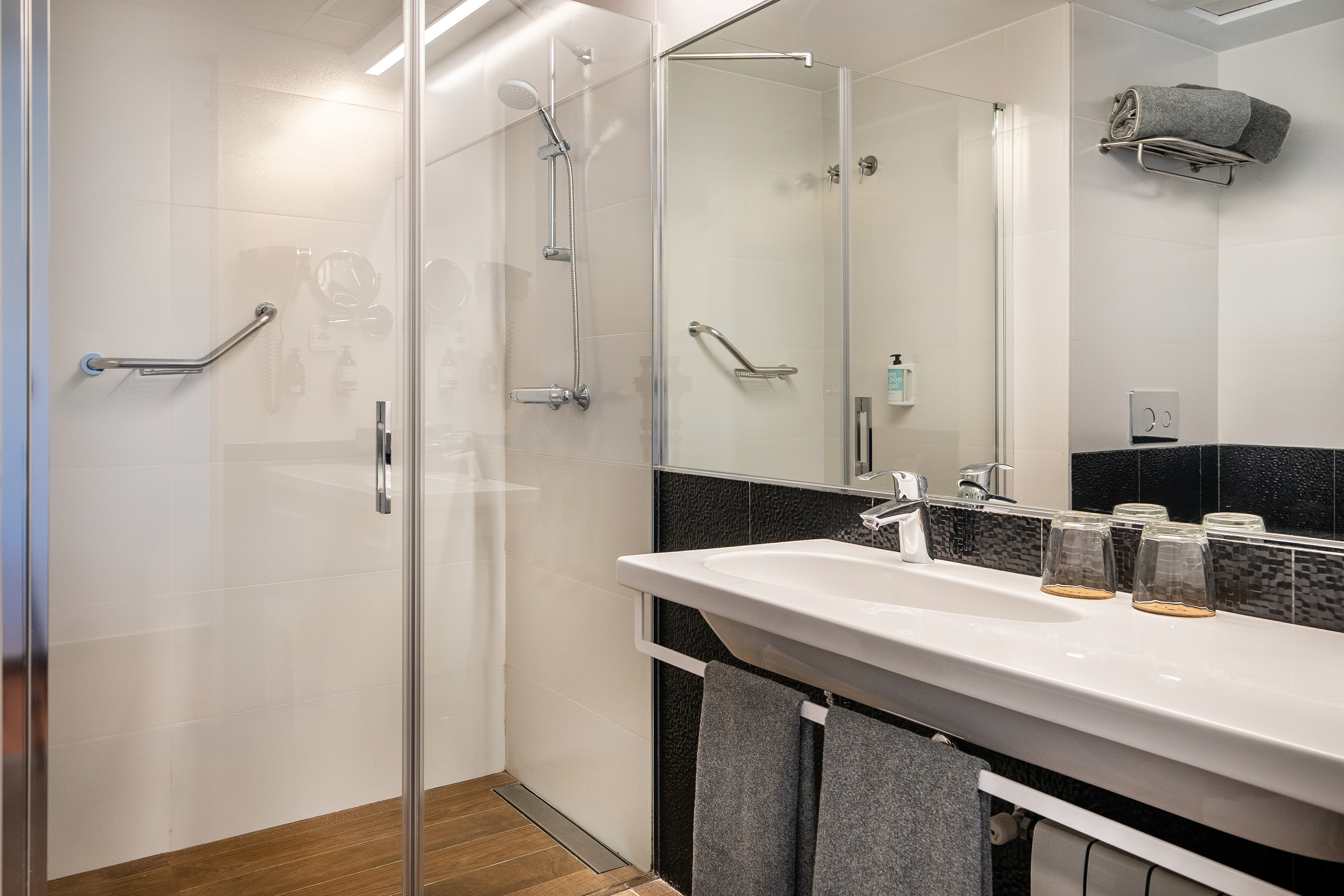 Accessible modern bathroom with walk-in shower, grab bar, white sink, wood floor.