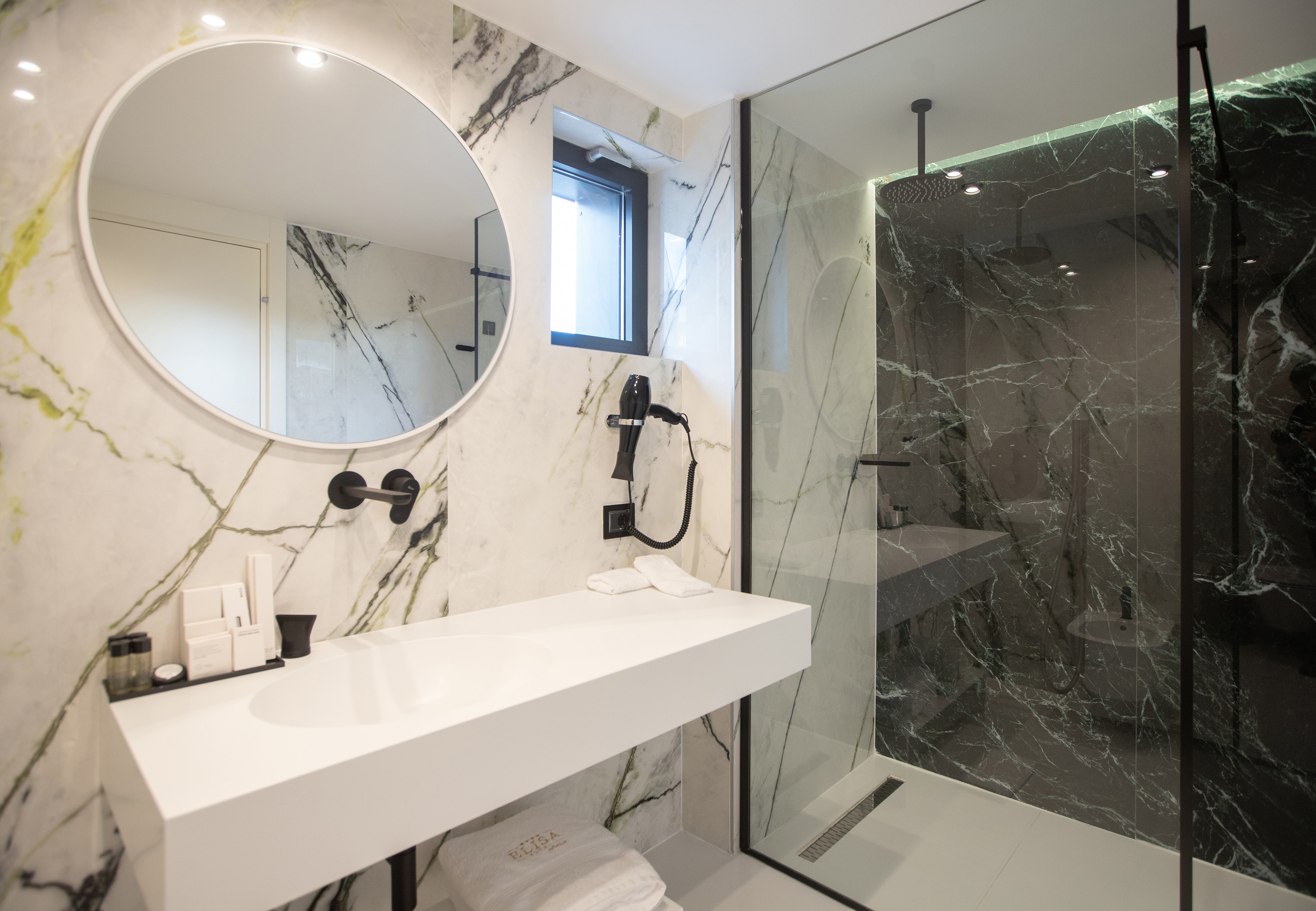 Modern bathroom with white and black marble, round mirror, and glass shower.