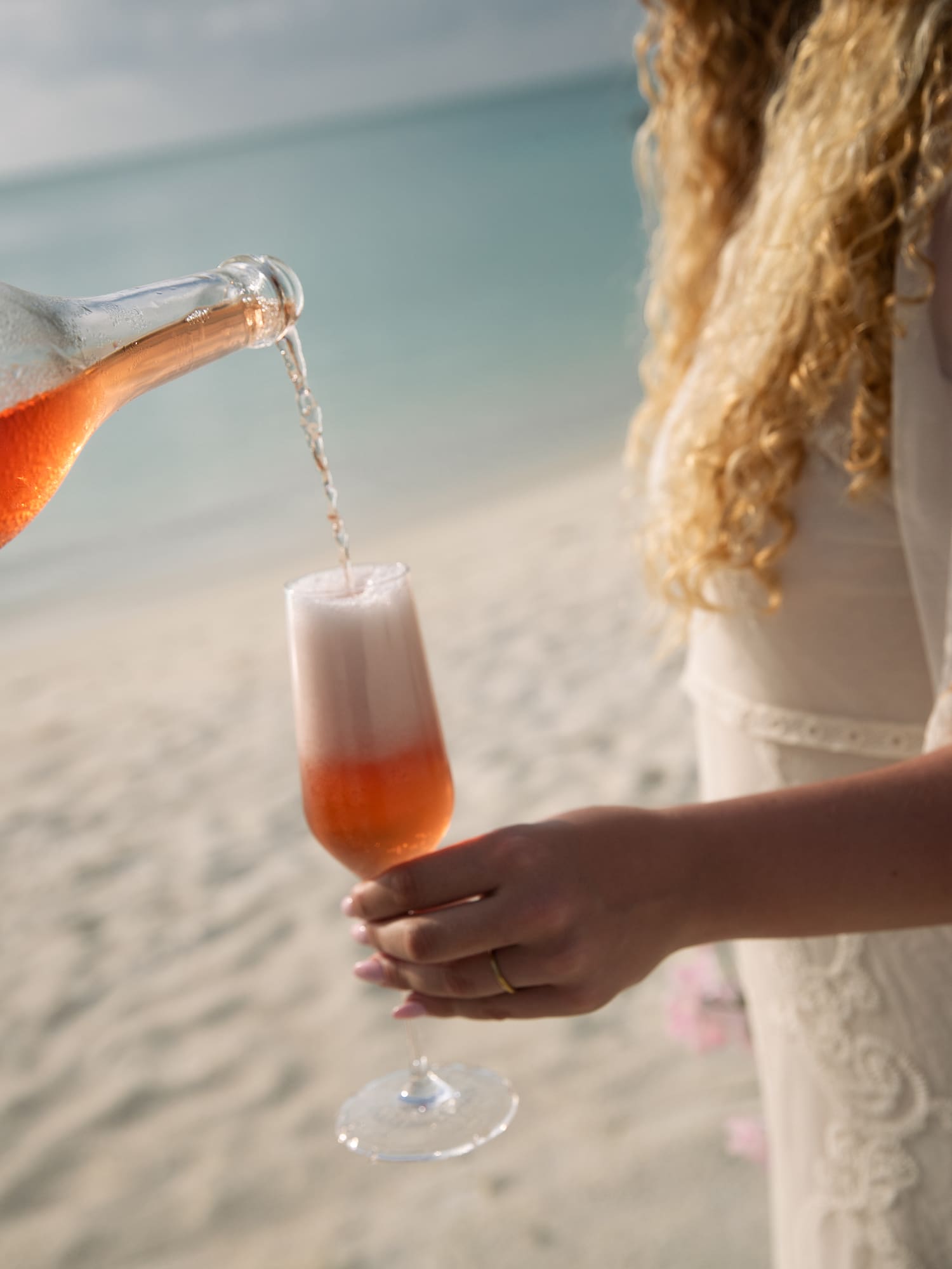 a woman pouring a drink into a glass on a beach