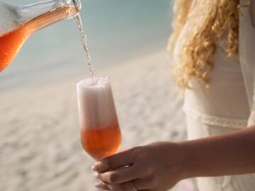 a woman pouring a drink into a glass on a beach