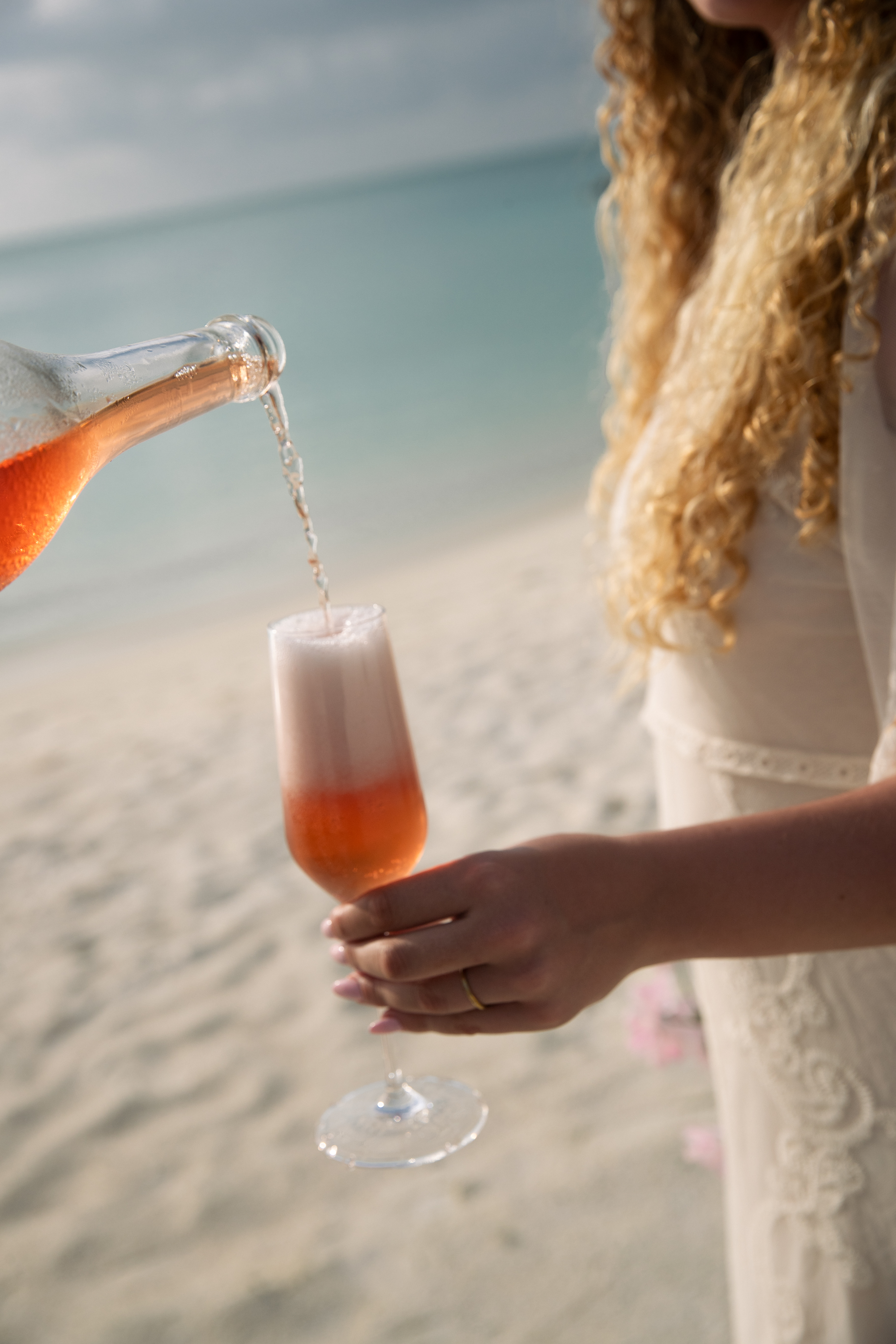 Hand pouring sparkling rosé into a flute on a tropical beach.