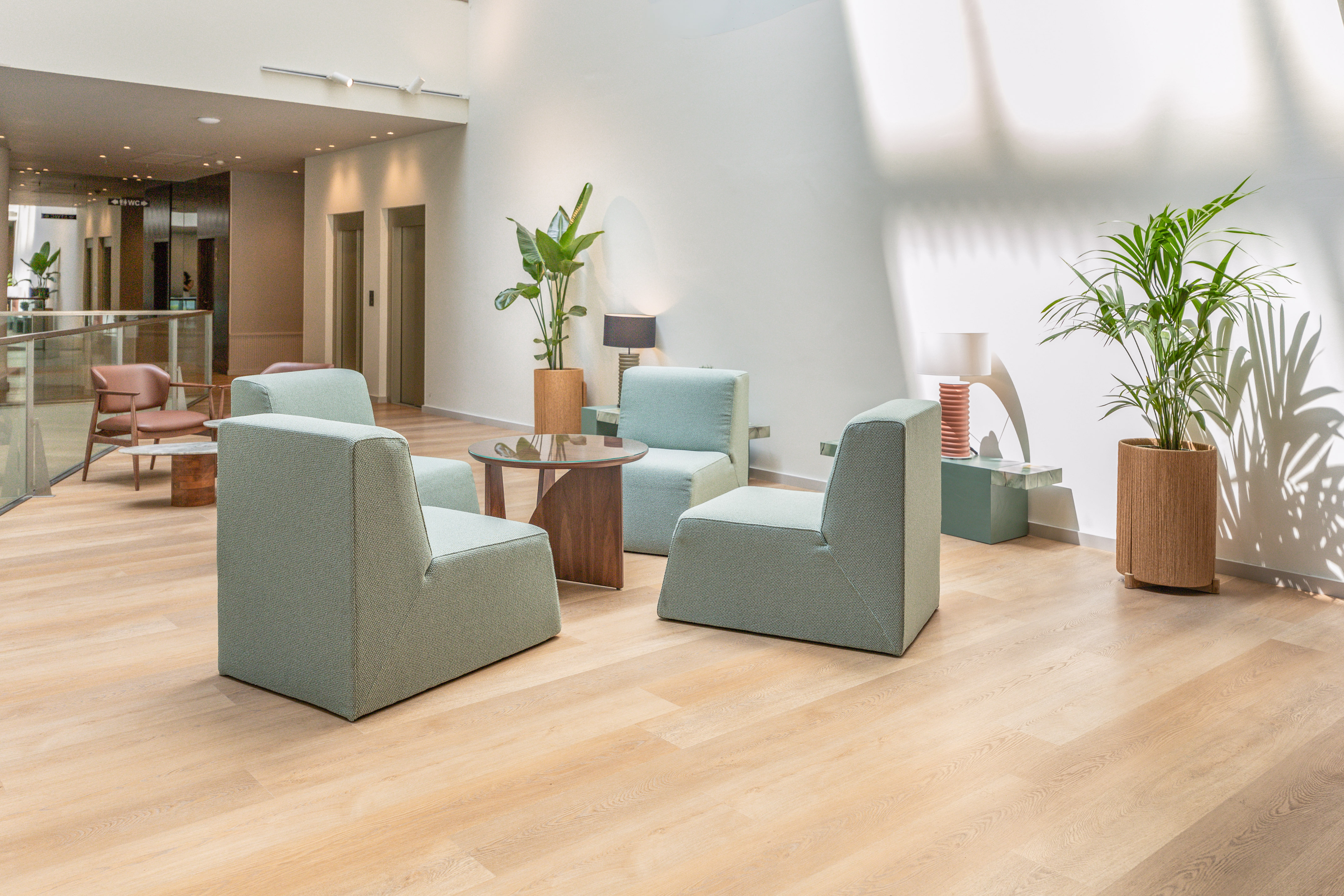Modern lobby with light green armchairs, wooden floor, and potted plants.