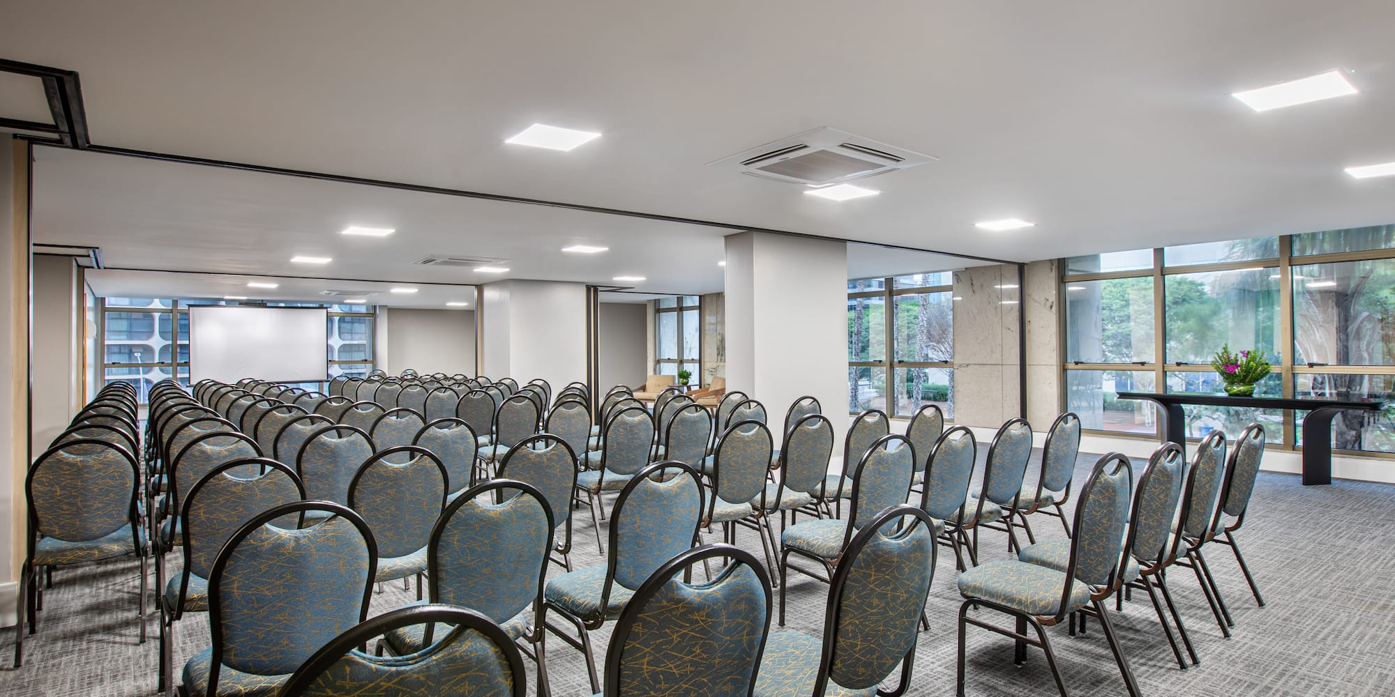 Conference room with empty blue chairs, projection screen, and large windows.