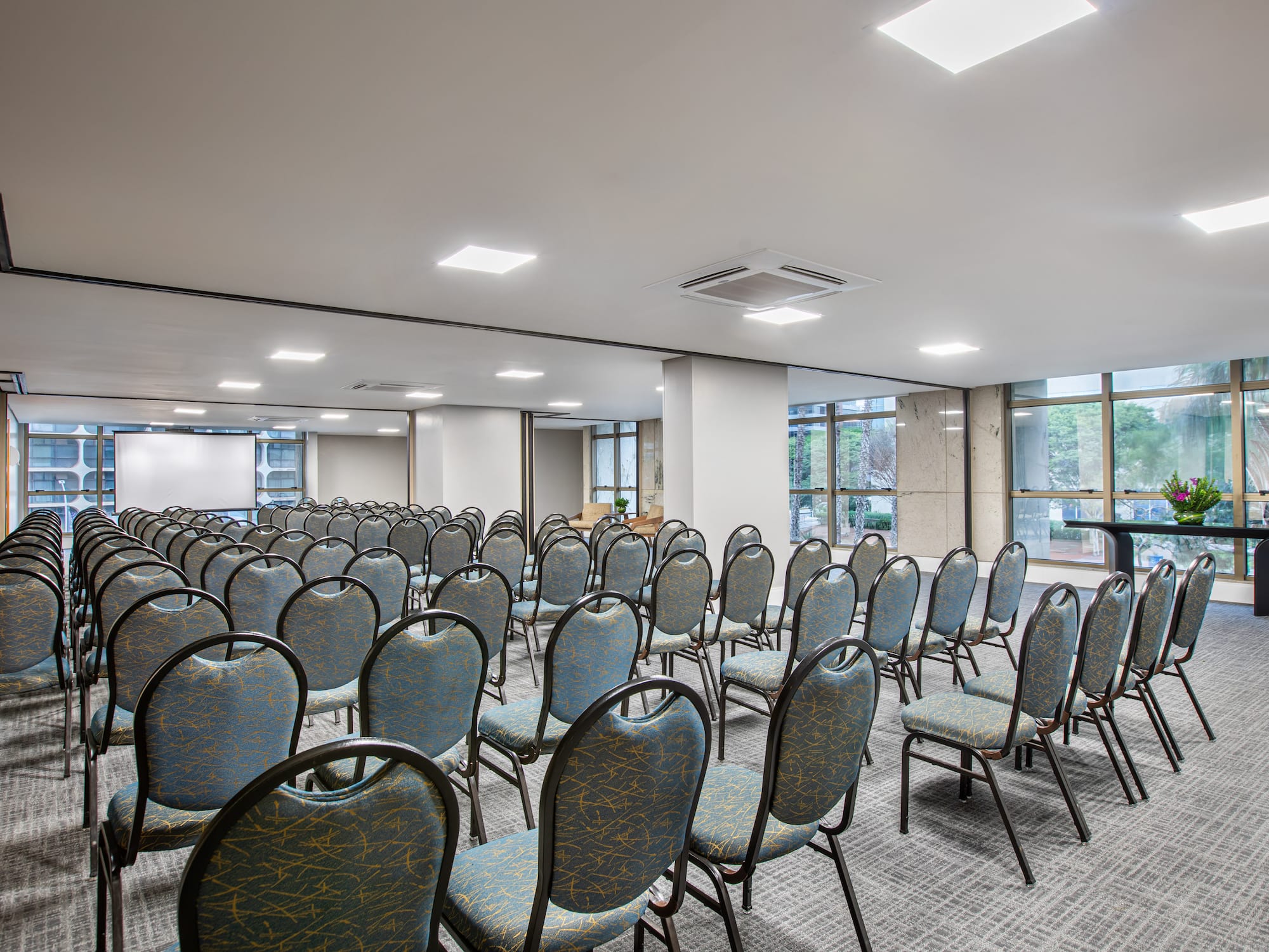 Empty modern event conference room with rows of chairs and screen.