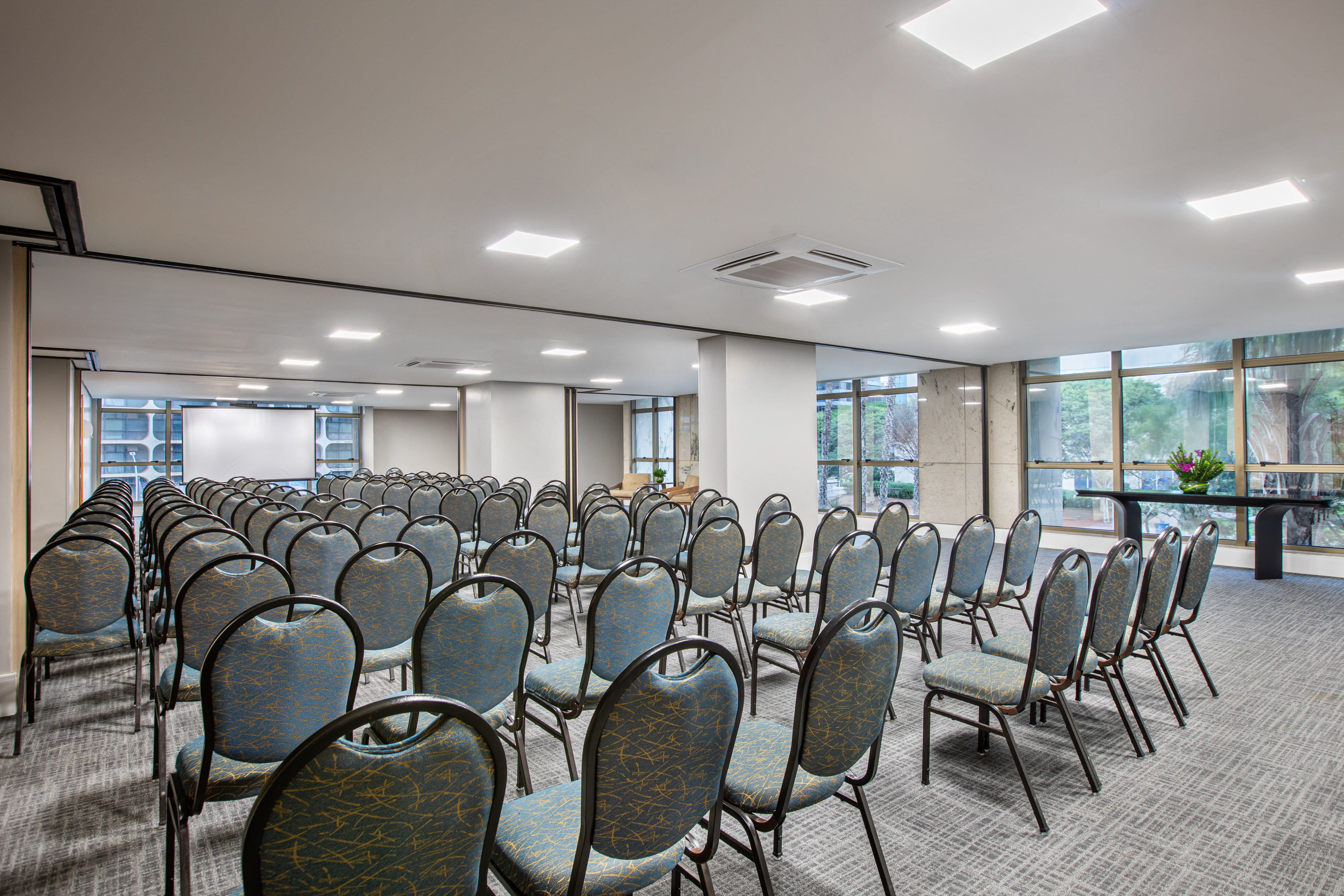 Conference room with empty blue chairs, projection screen, and large windows.