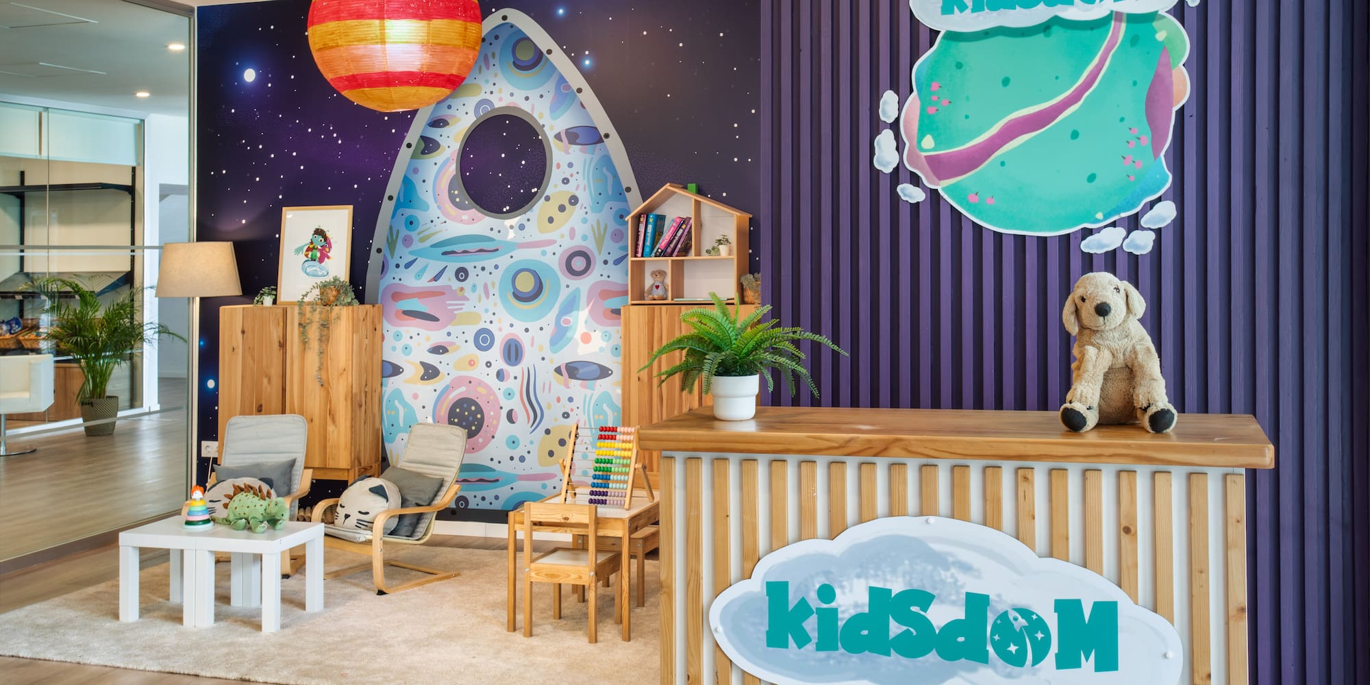 KidsDóM colorful space-themed kids' play area and reception with wooden desk.