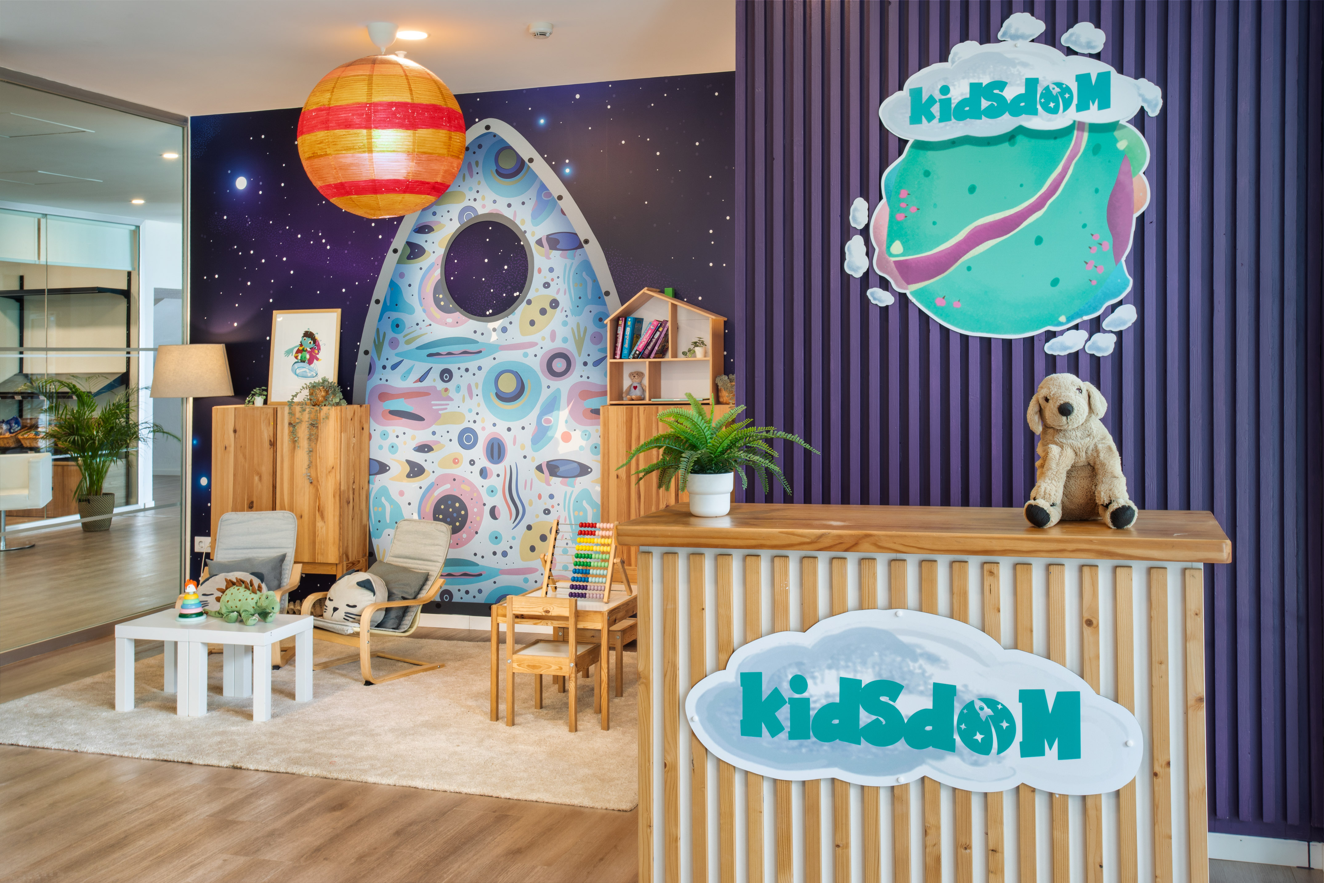 KidsDóM colorful space-themed kids' play area and reception with wooden desk.