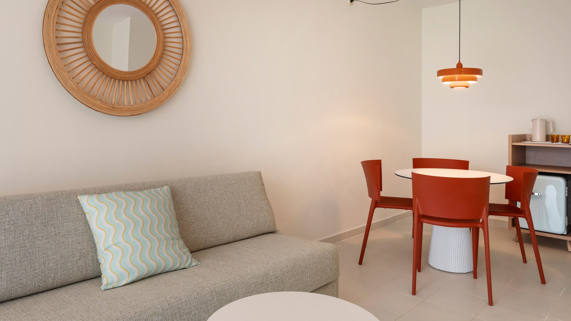 Modern living area with gray sofa, wooden mirror, and orange dining set.