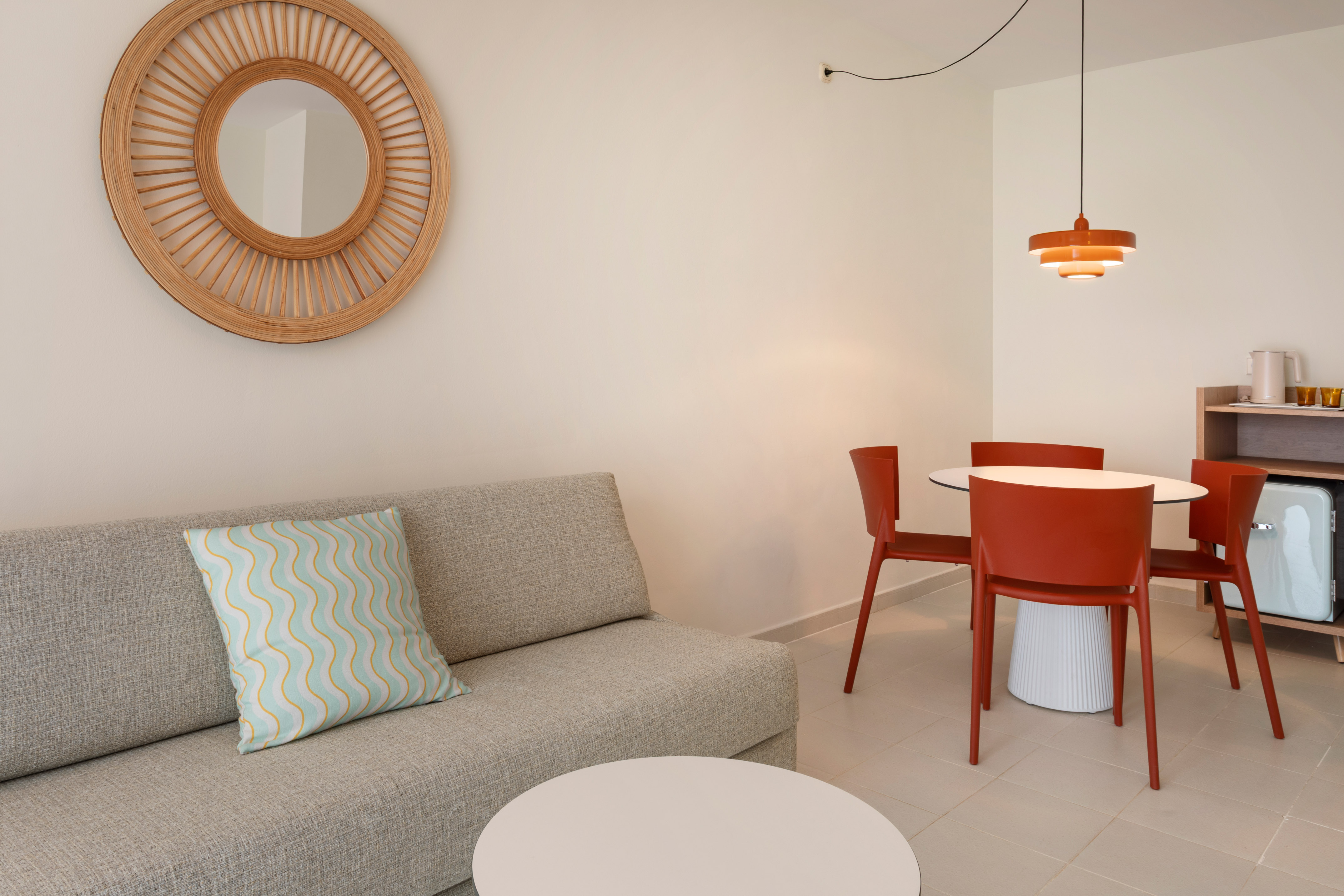 Modern living area with gray sofa, wooden mirror, and orange dining set.