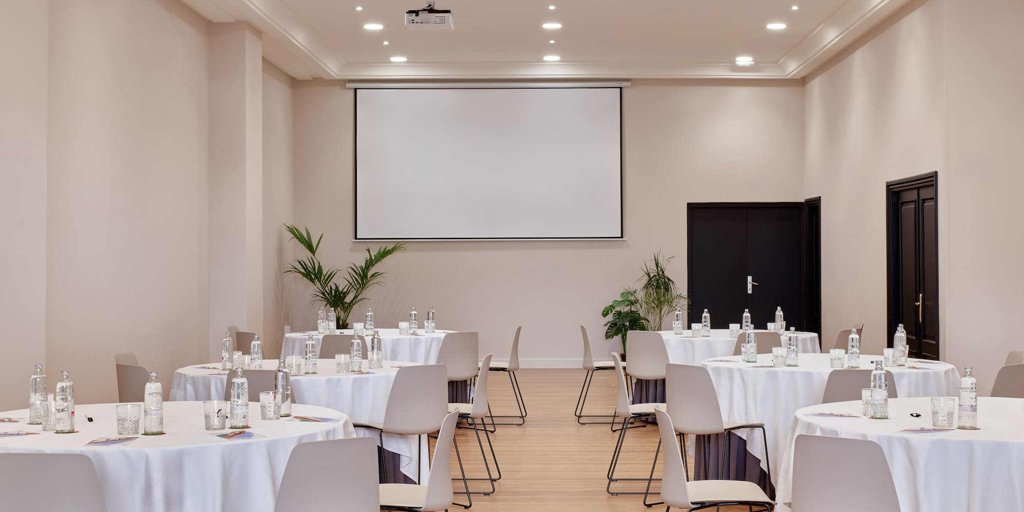 Spacious meeting room with projector screen, round tables, and modern chairs.