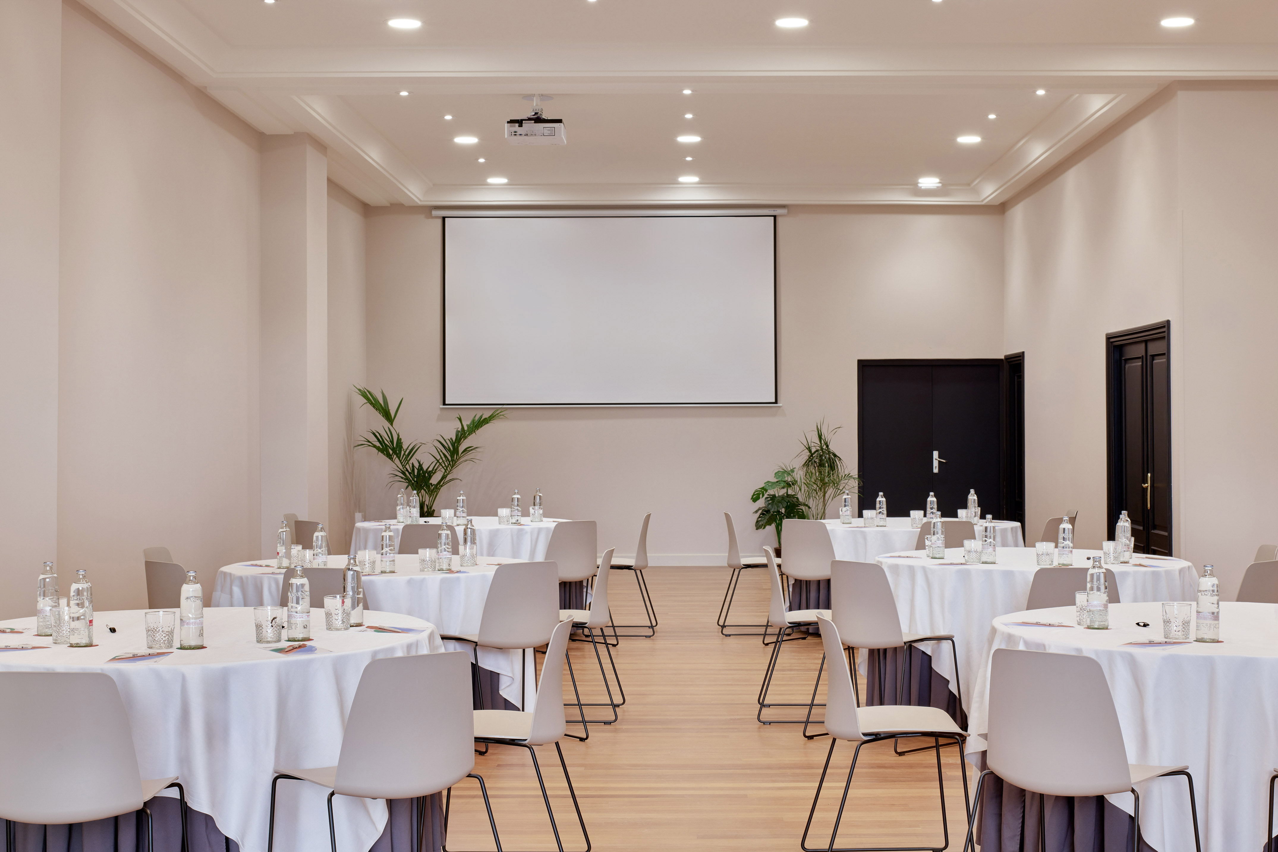 Spacious meeting room with projector screen, round tables, and modern chairs.