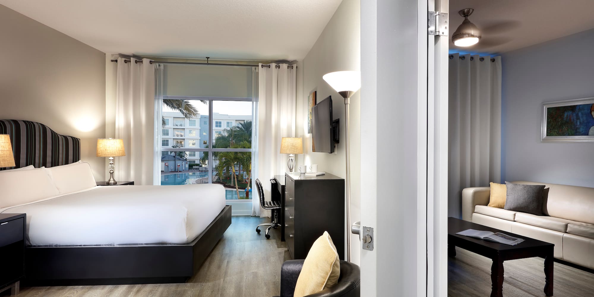 Modern hotel suite with king bed, pool view, and adjoining living room.